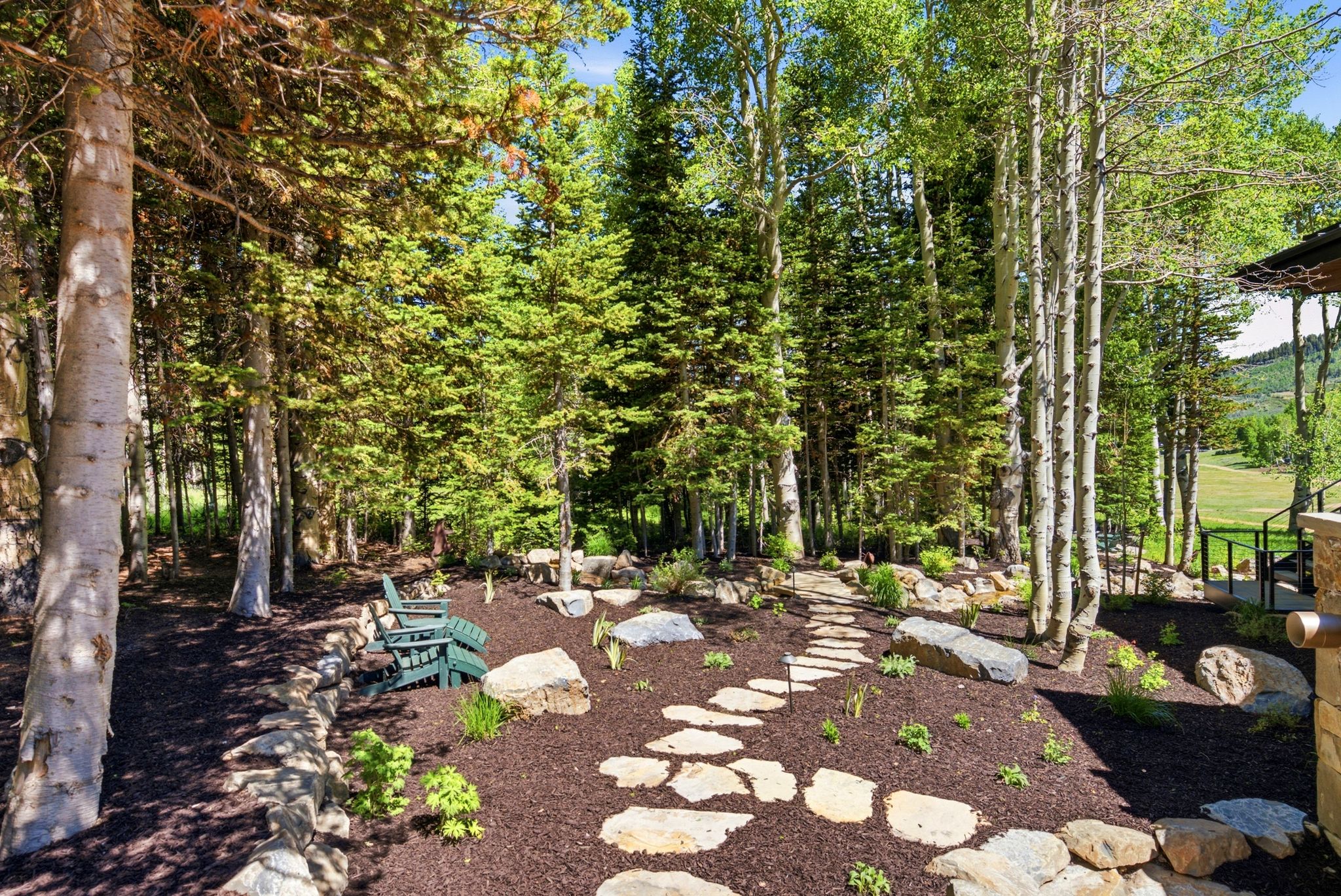 Wooded exterior landscaping featuring mature evergreen and aspen trees, a stone retaining wall, and a stepping stone pathway