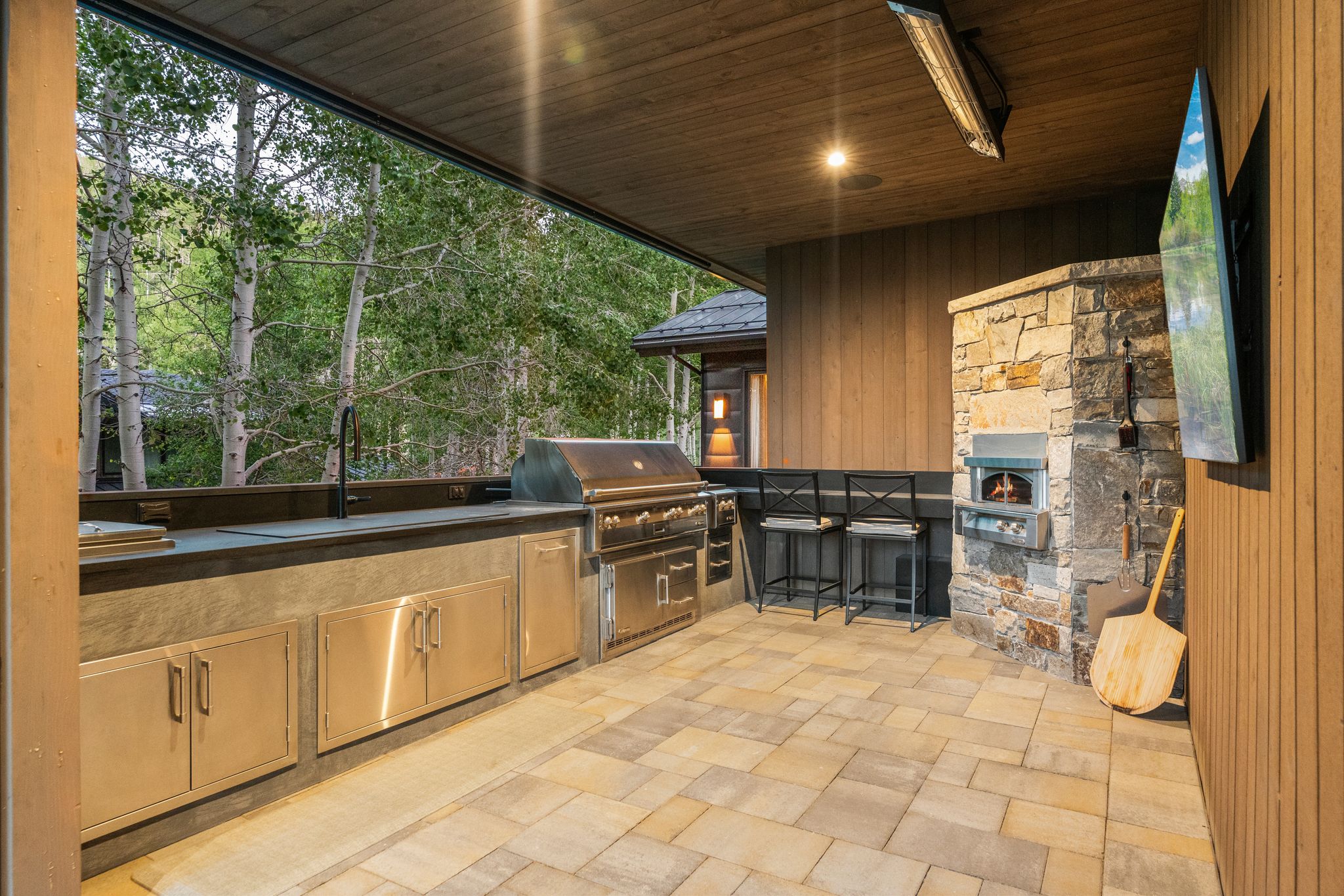 Covered outdoor kitchen featuring a built-in grill, stone pizza oven, and stainless steel cabinetry