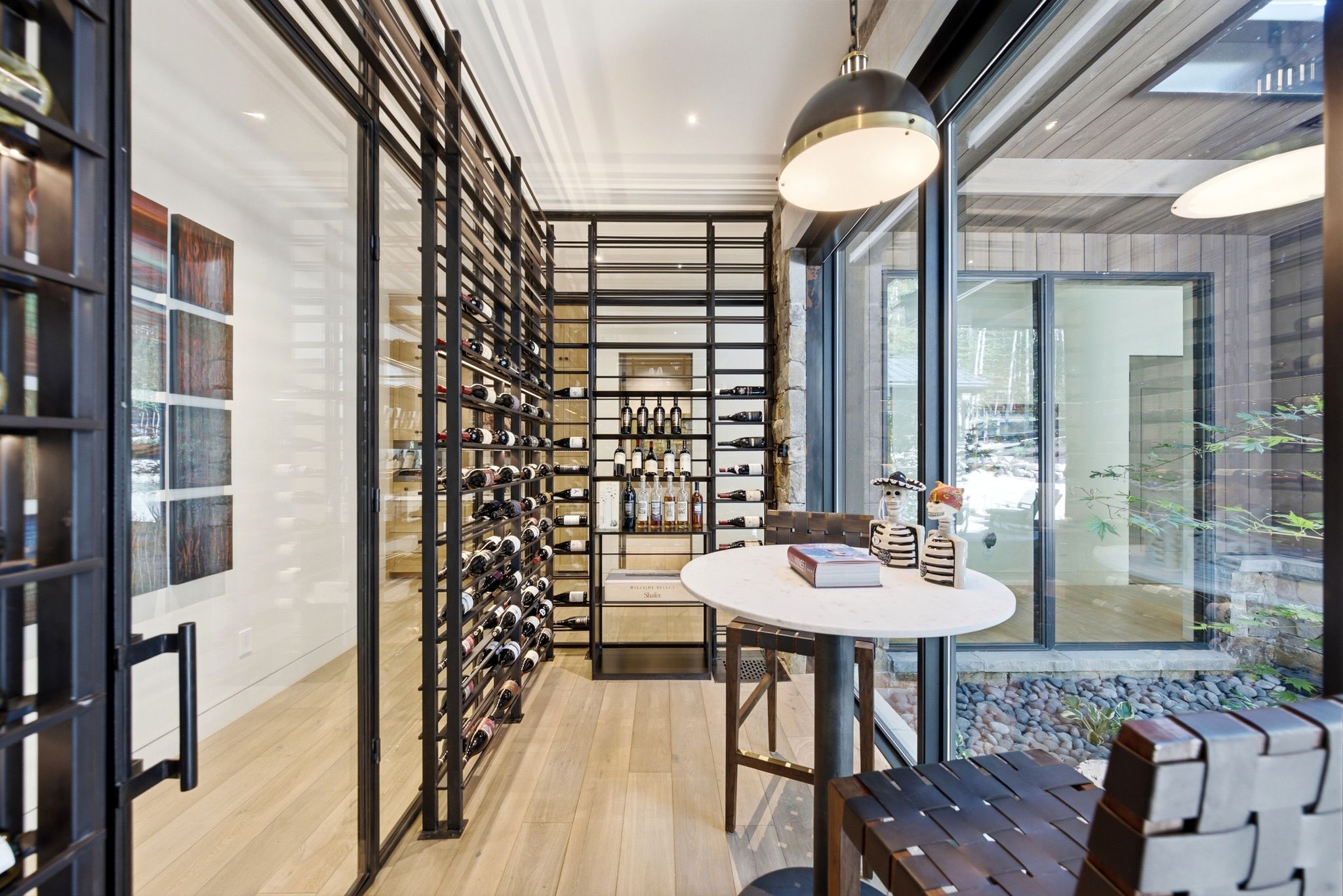 Dedicated wine room featuring floor-to-ceiling glass and metal wine racks, light wood-finish flooring, and a contemporary pendant light fixture