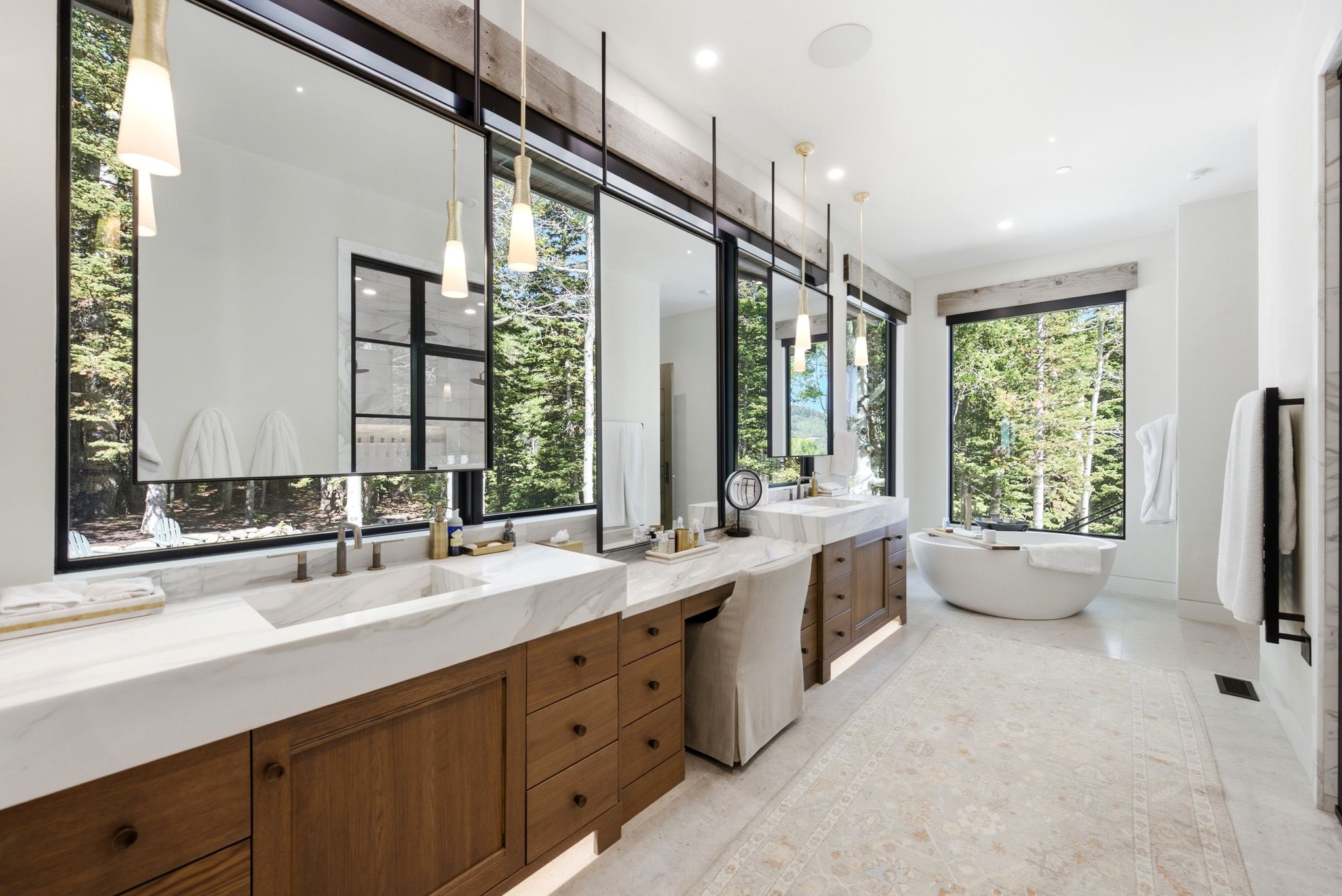 Spacious bathroom featuring a freestanding soaking tub, wood vanities with integrated sinks, and large windows