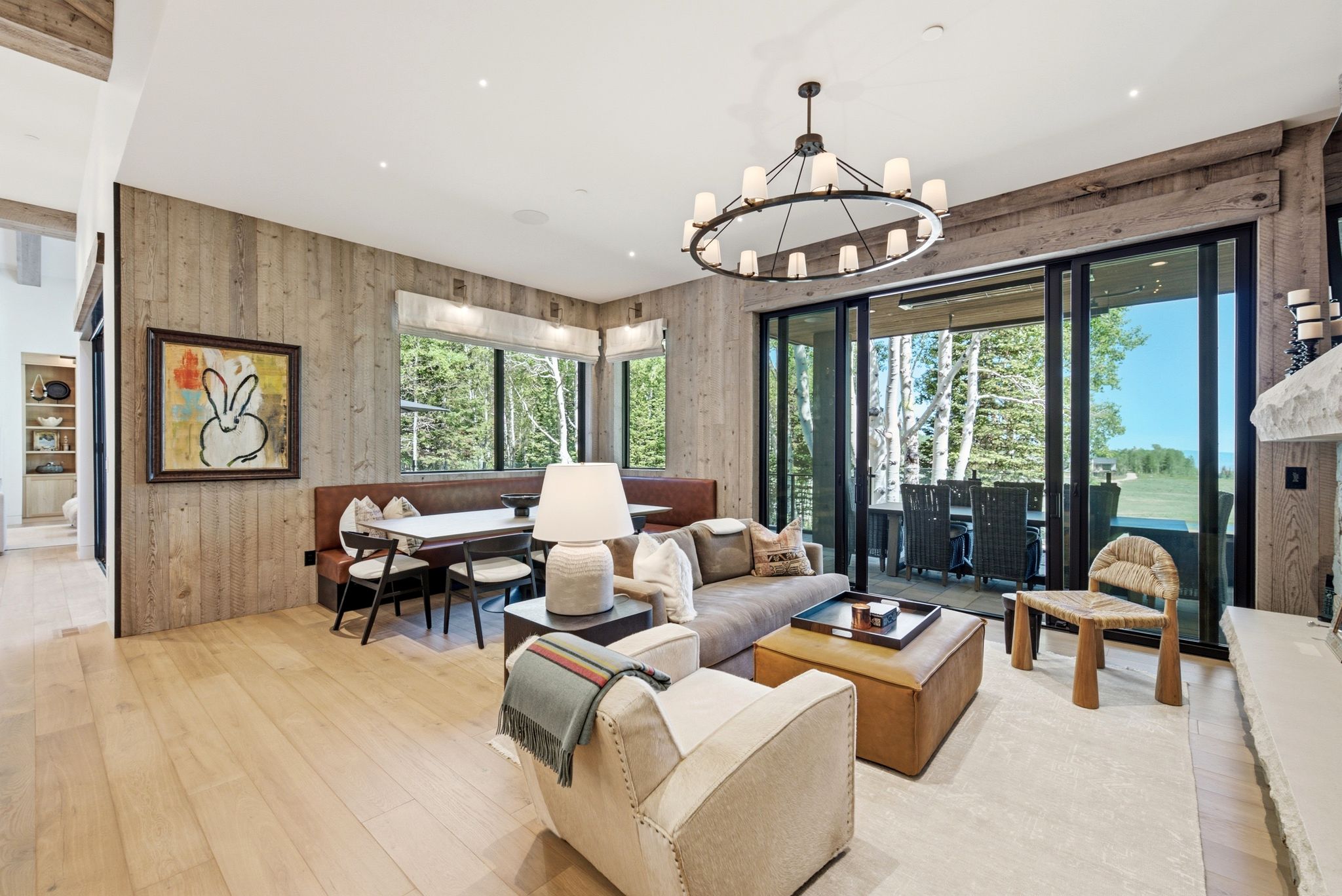 Living area featuring light wood-finish flooring, accent wood-paneled walls, an integrated dining nook, expansive glass sliding doors, and an outdoor patio