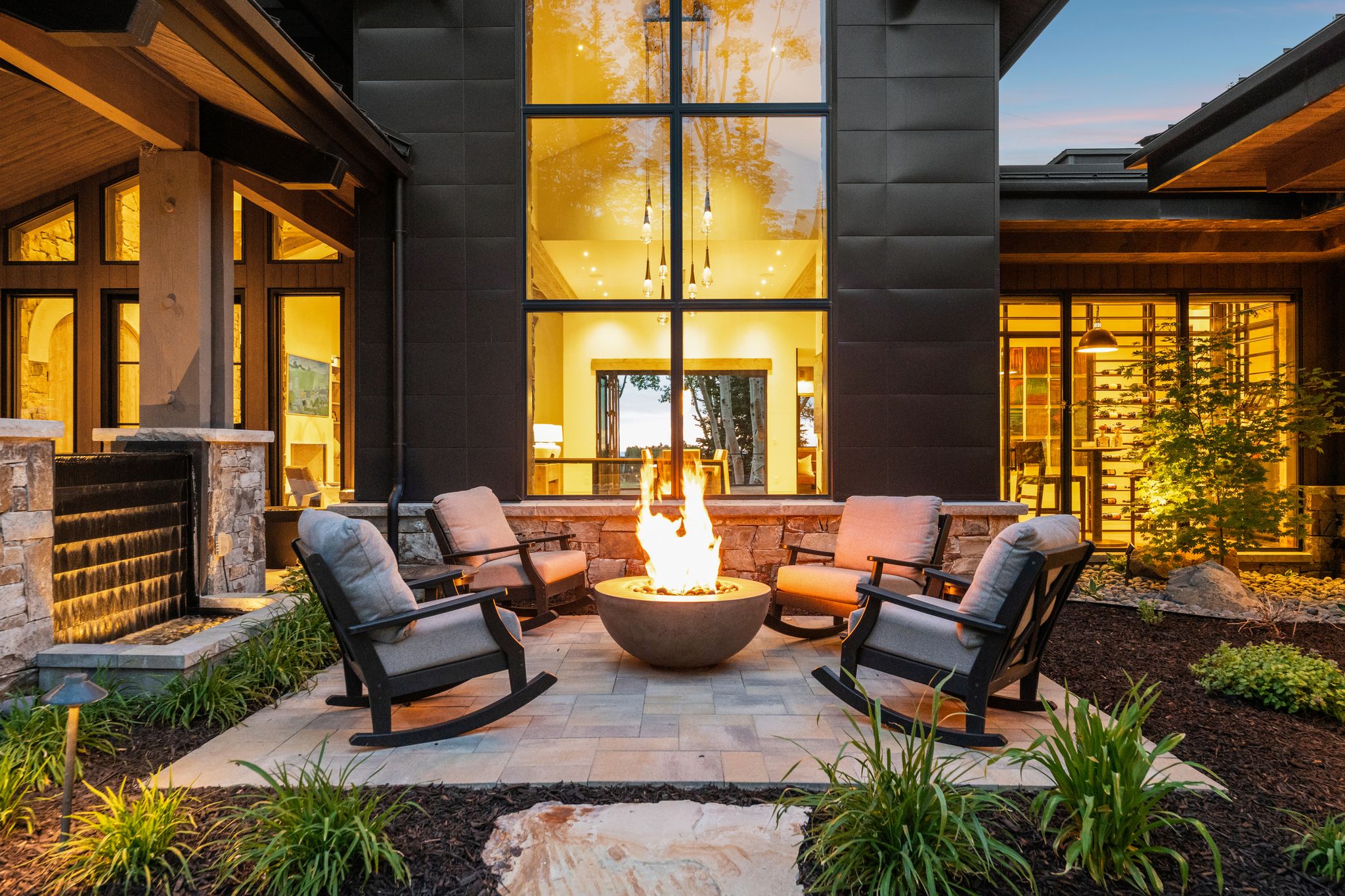 Outdoor patio with a circular fire pit, paver flooring, stone accent walls, a water feature, and large windows