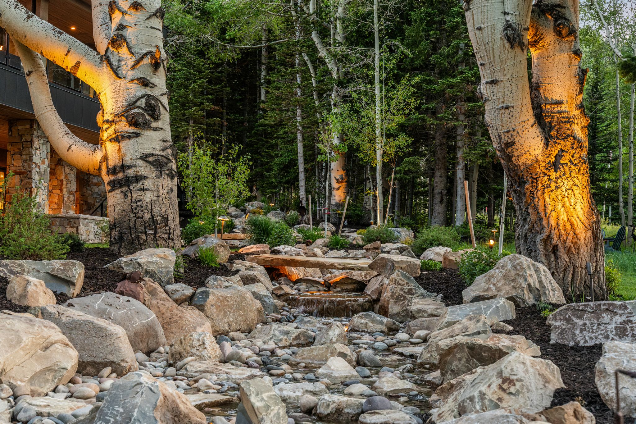 Stone-lined water feature with multiple cascades, surrounded by natural boulders and mature aspen trees