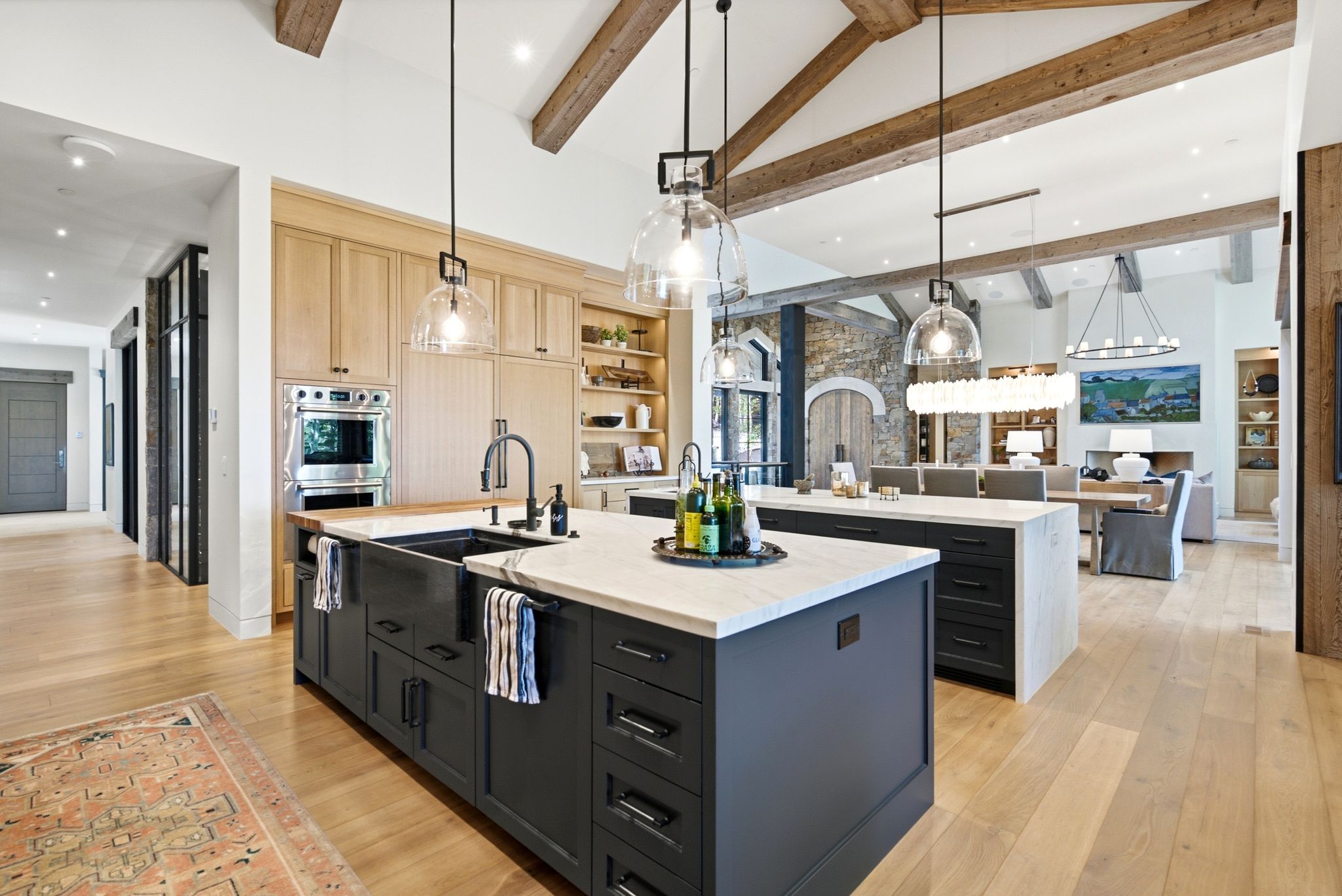 Gourmet kitchen featuring dual islands with stone countertops, a large farmhouse-style sink, integrated appliances, and light wood-finish cabinetry