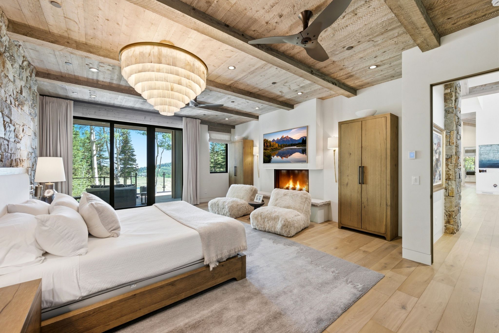 Spacious bedroom featuring a stone accent wall, wood-finish ceiling with exposed beams, and a large sliding glass door opening to an exterior area