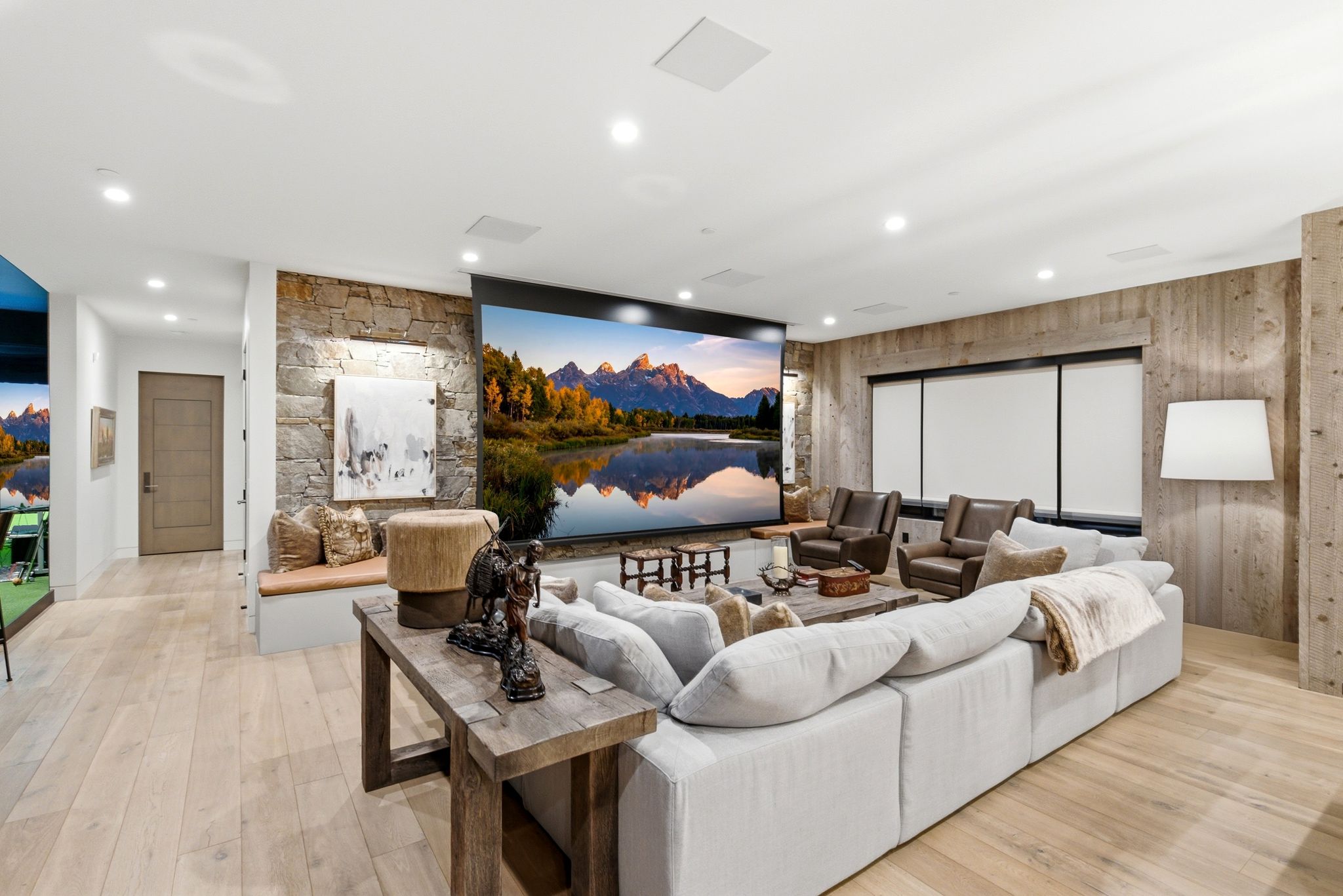 Entertainment space featuring a large projection screen, stone accent wall, wood-finish flooring, recessed lighting, and integrated ceiling speakers