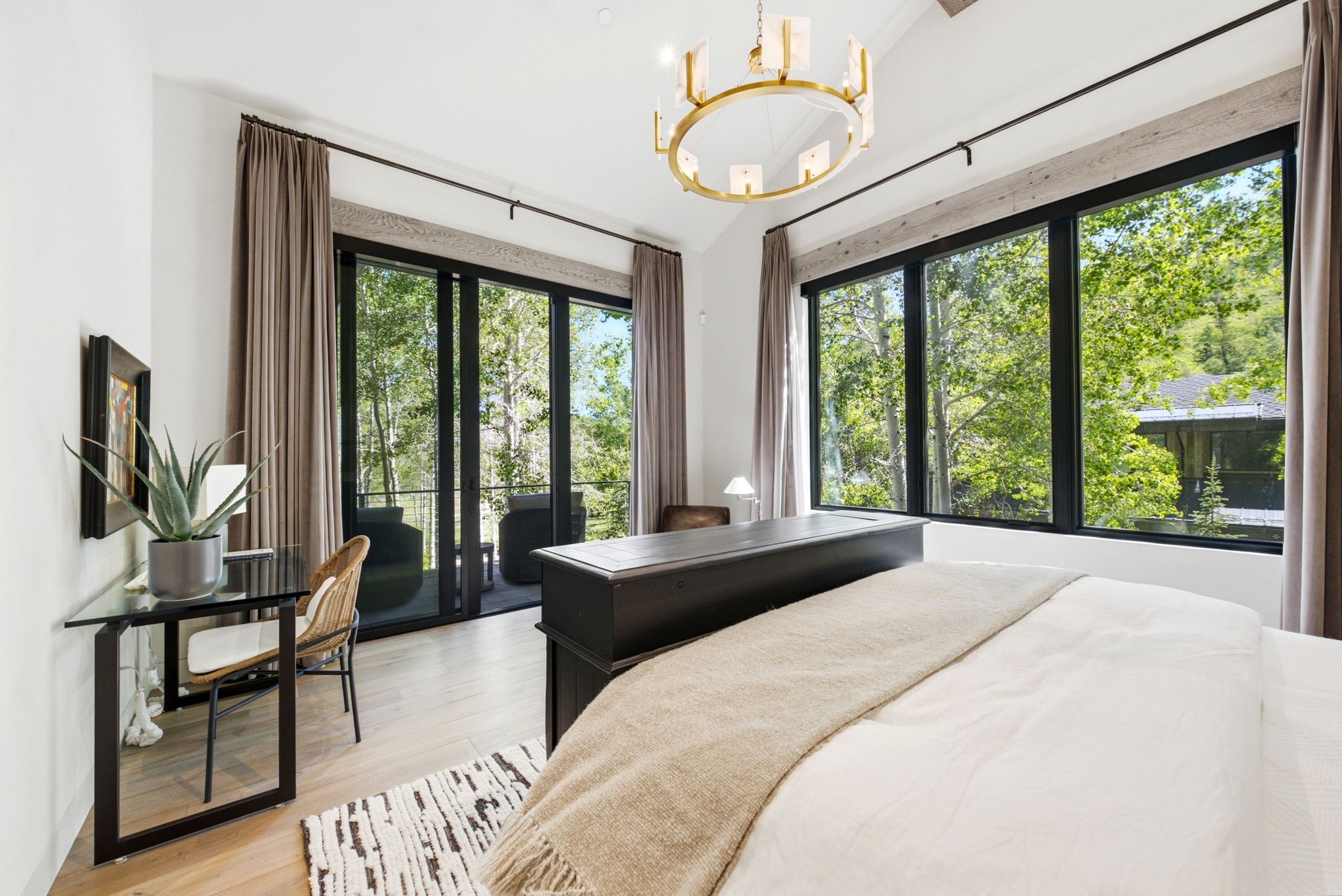 Vaulted ceiling bedroom featuring large windows, a sliding glass door to an outdoor balcony, wood-finish flooring, and a contemporary circular chandelier