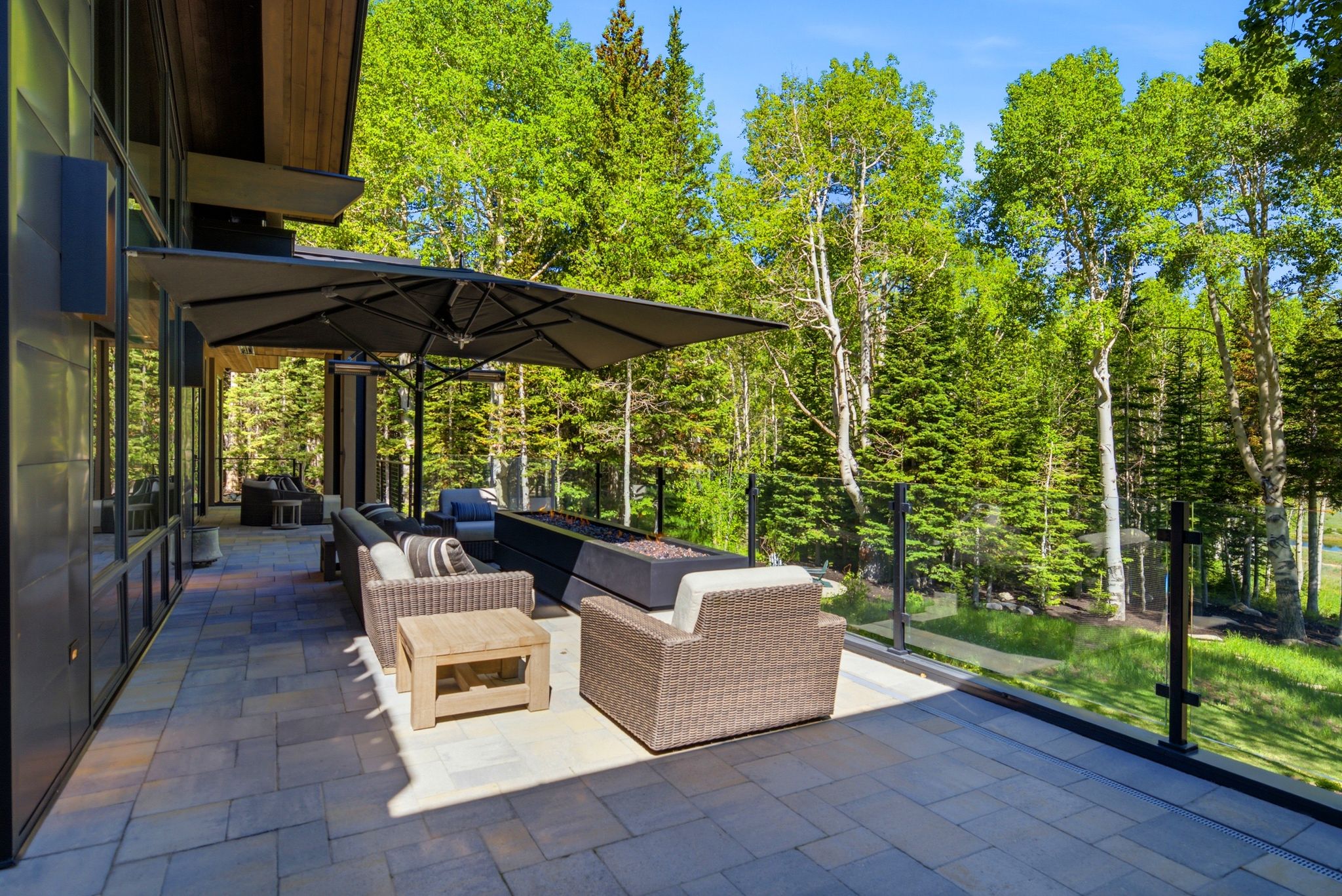 Spacious outdoor patio featuring paver flooring, a glass railing, and a built-in linear fire pit