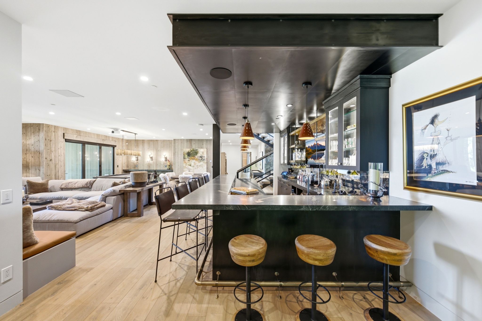 Expansive entertainment space featuring a built-in bar with dark cabinetry and a stone countertop, light wood-finish flooring, and recessed lighting