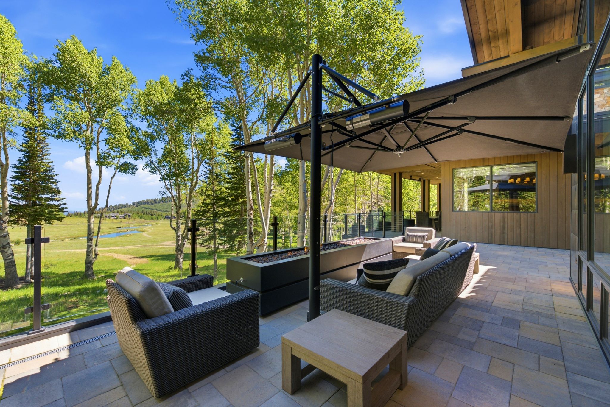Expansive patio featuring multi-tone paver flooring, a perimeter glass railing, and a built-in fire feature