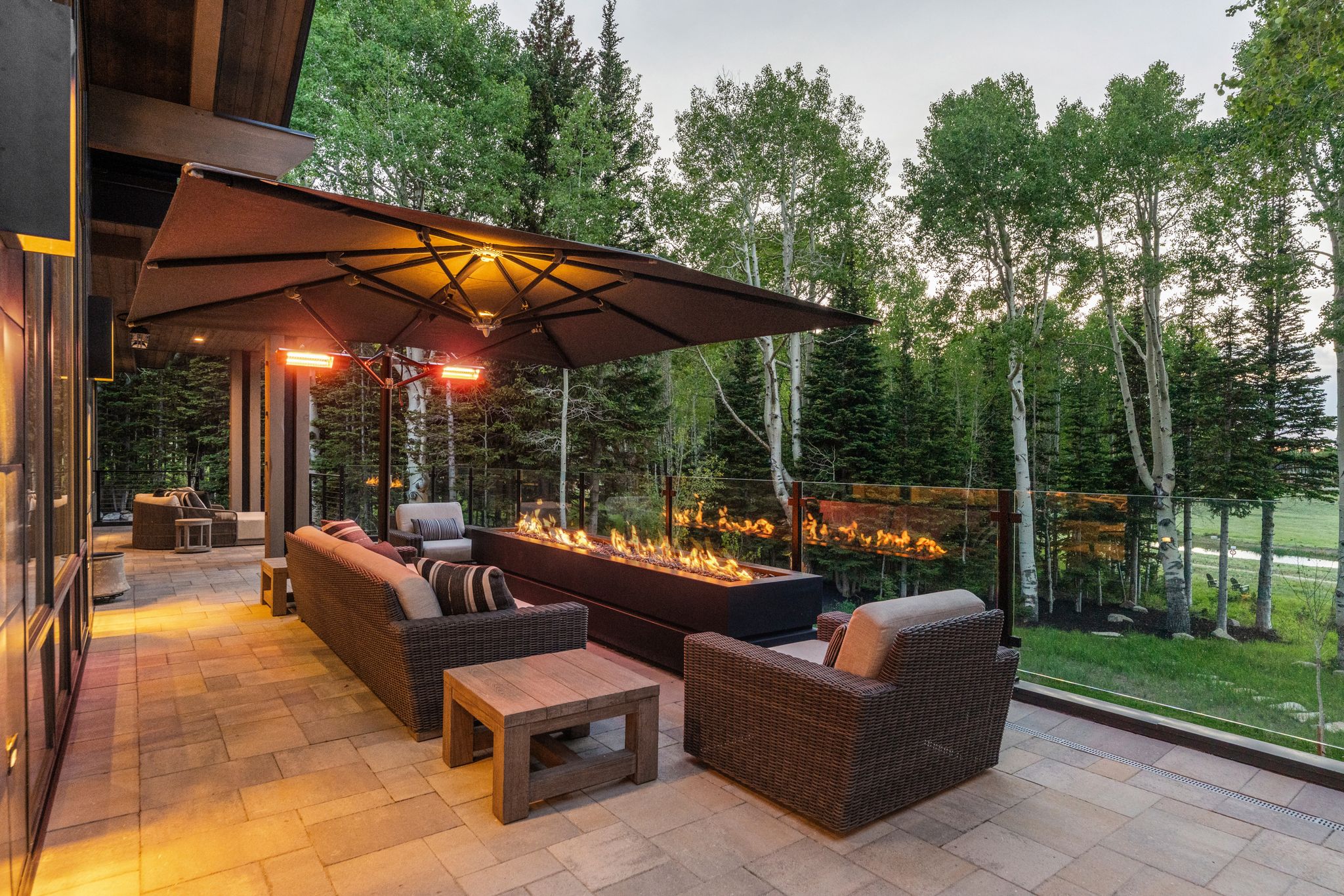 Expansive patio featuring paver flooring, a glass railing, and a linear fire pit