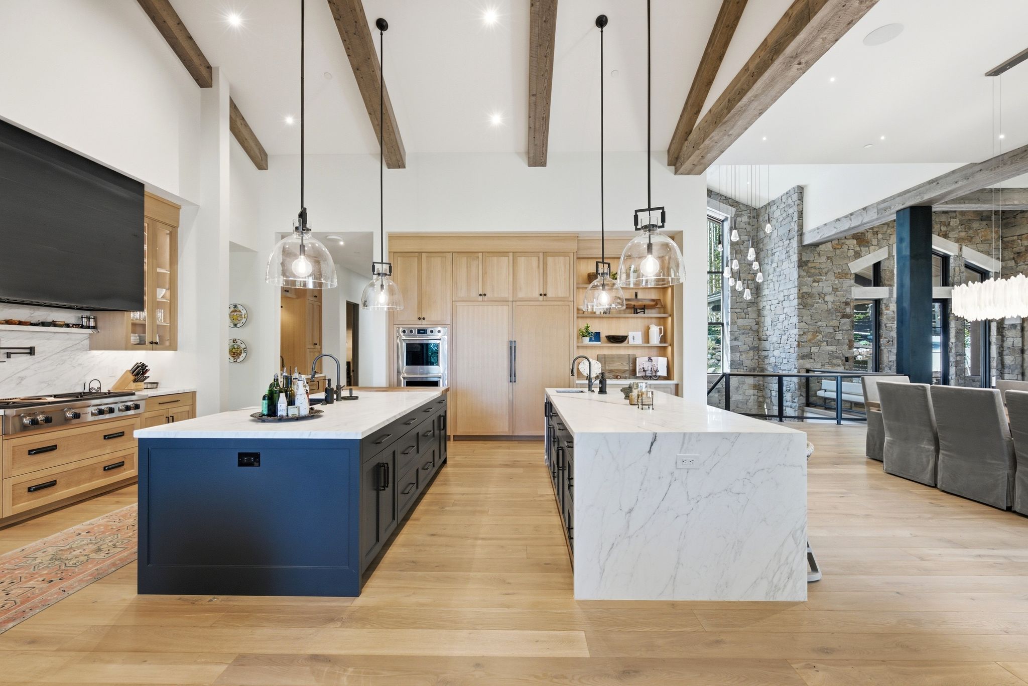 Gourmet kitchen featuring two expansive islands with stone countertops, a professional-grade range with hood, integrated appliances, and exposed wood ceiling beams