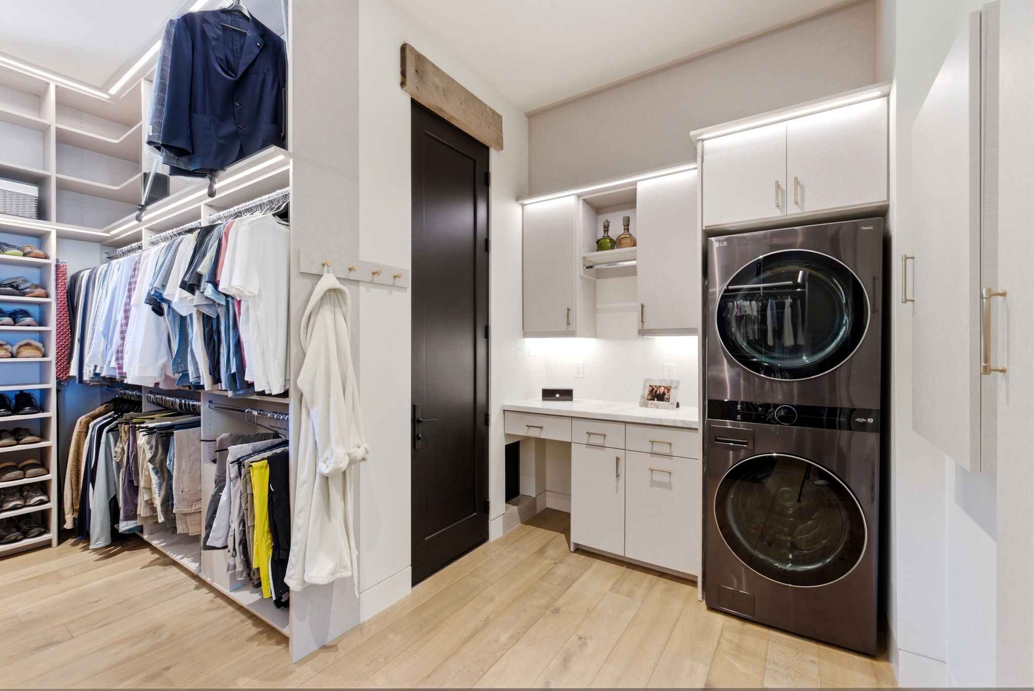 Integrated laundry area featuring stacked front-load machines, custom cabinetry with under-cabinet lighting, and a durable countertop