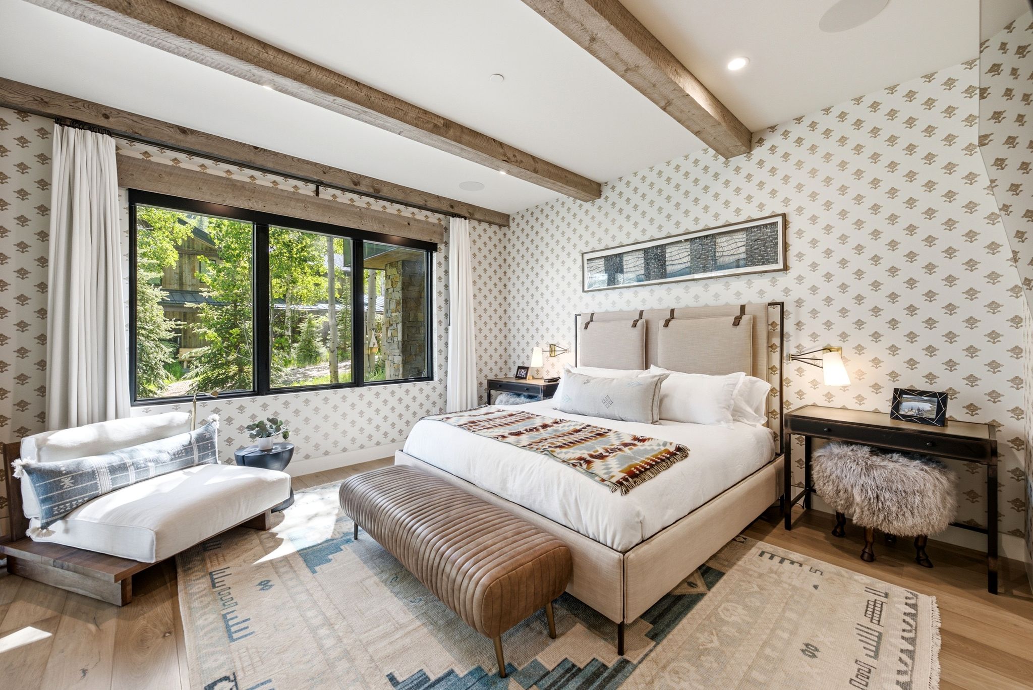 Spacious bedroom featuring light wood-finish flooring, exposed ceiling beams, and patterned wallcovering