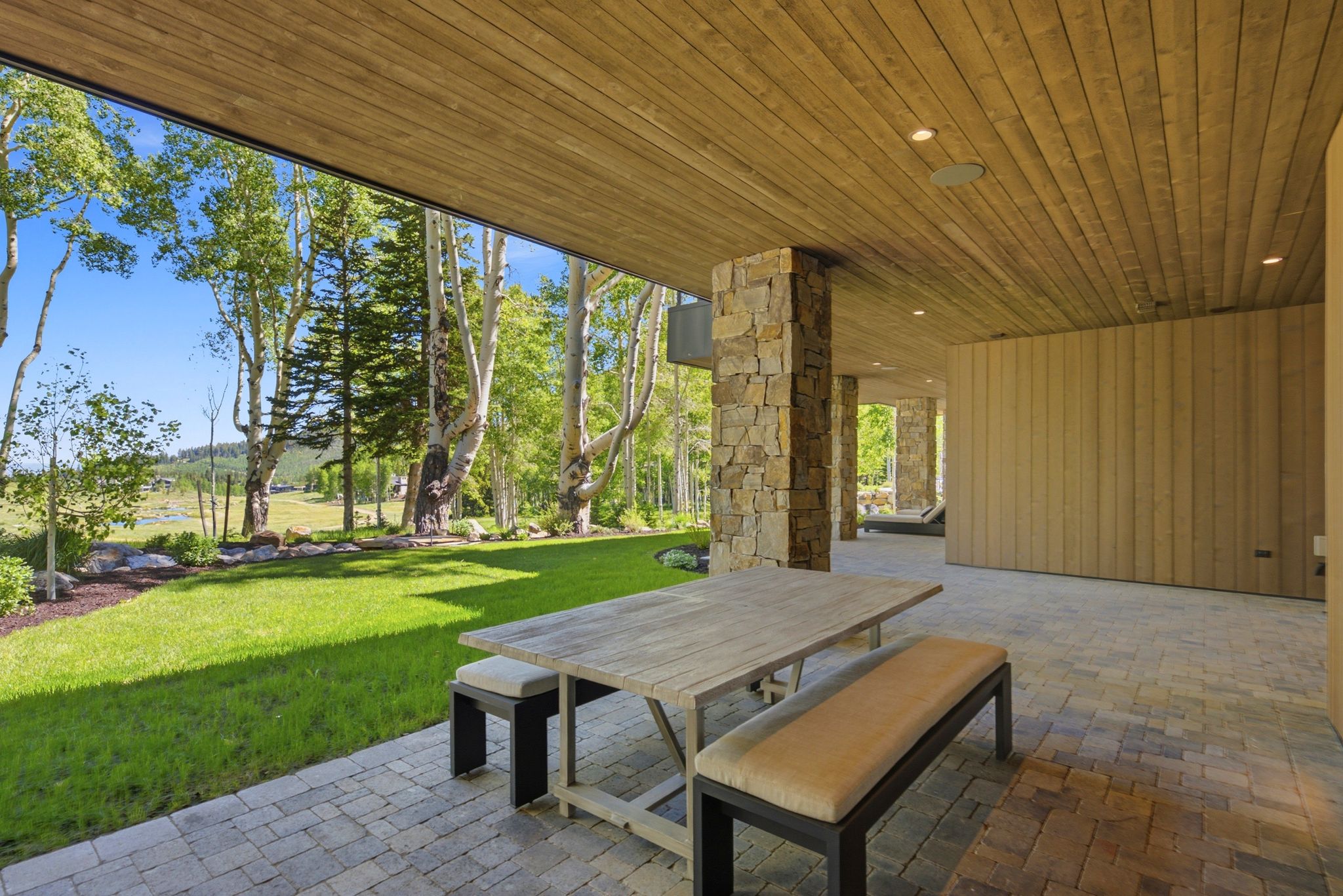 Expansive covered patio featuring a paver surface, wood-finish ceiling, recessed lighting, and a stone-clad column