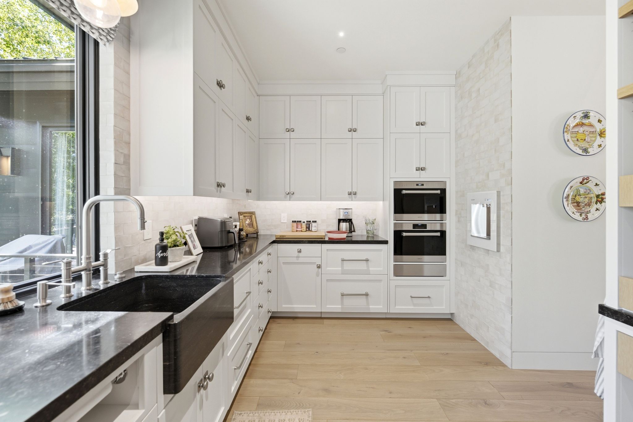 Modern kitchen featuring white cabinetry with silver hardware, black stone countertops, and a black farmhouse sink with a gooseneck faucet