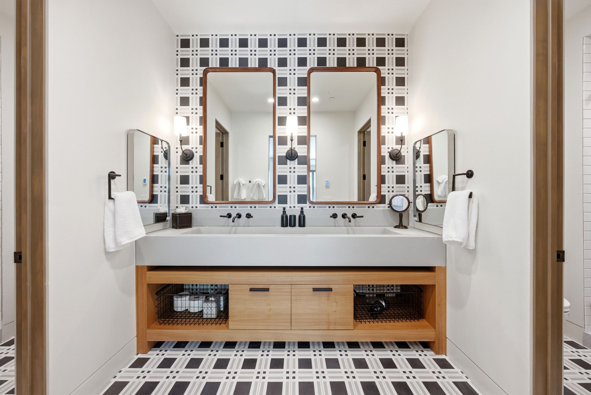 Dual vanity featuring an integrated sink, wall-mounted matte black faucets, and a light wood-finish base with open shelving and drawer storage