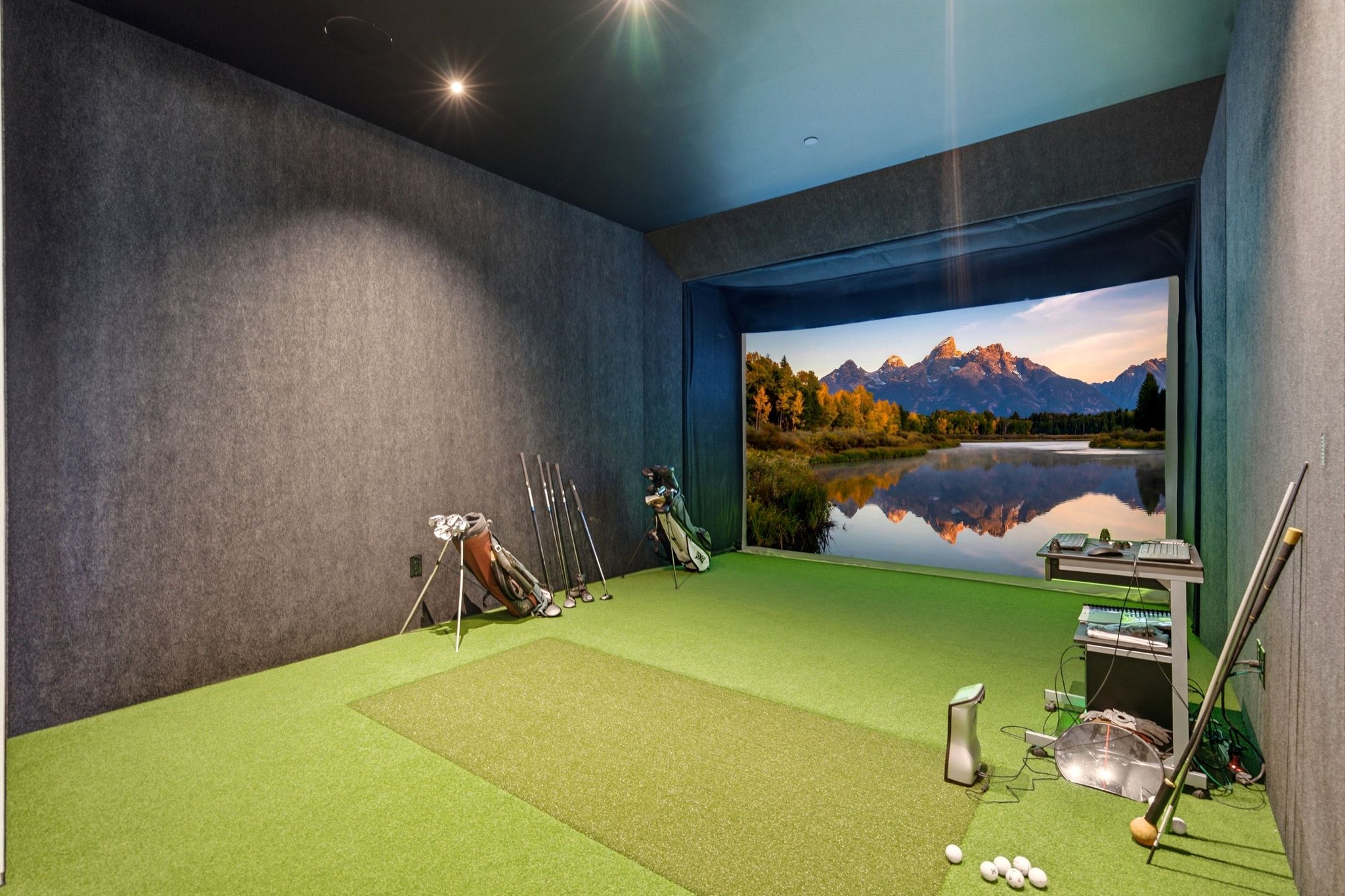 Dedicated golf simulator room featuring a wide projection screen, artificial turf flooring, and sound-absorbing wall treatments
