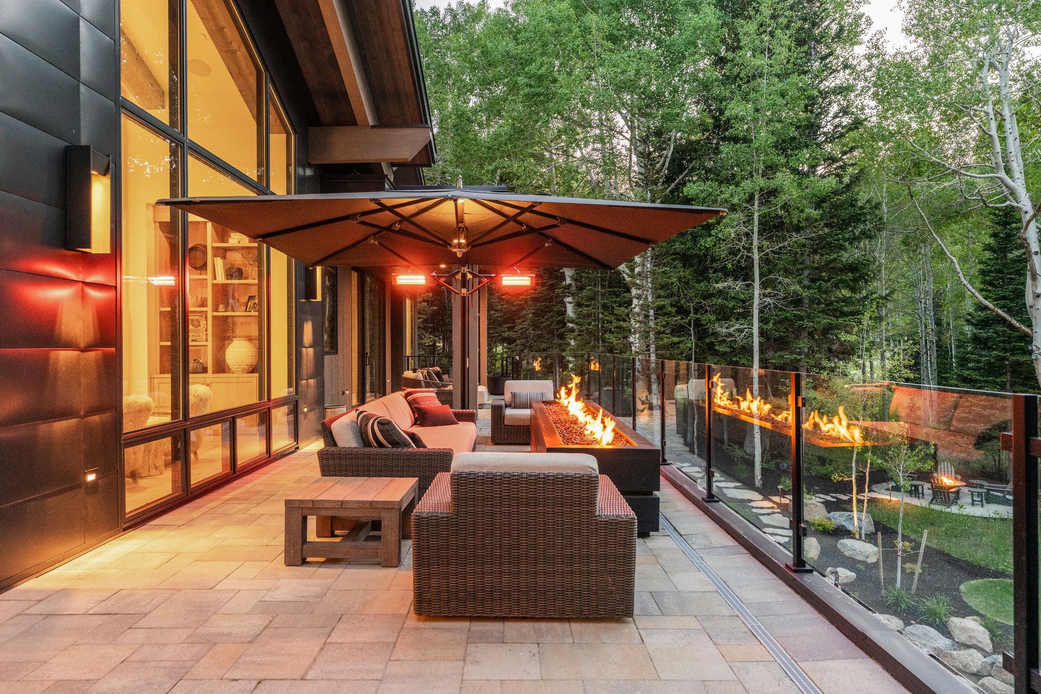 Expansive outdoor living patio featuring paver flooring, a linear fire pit, and glass railing