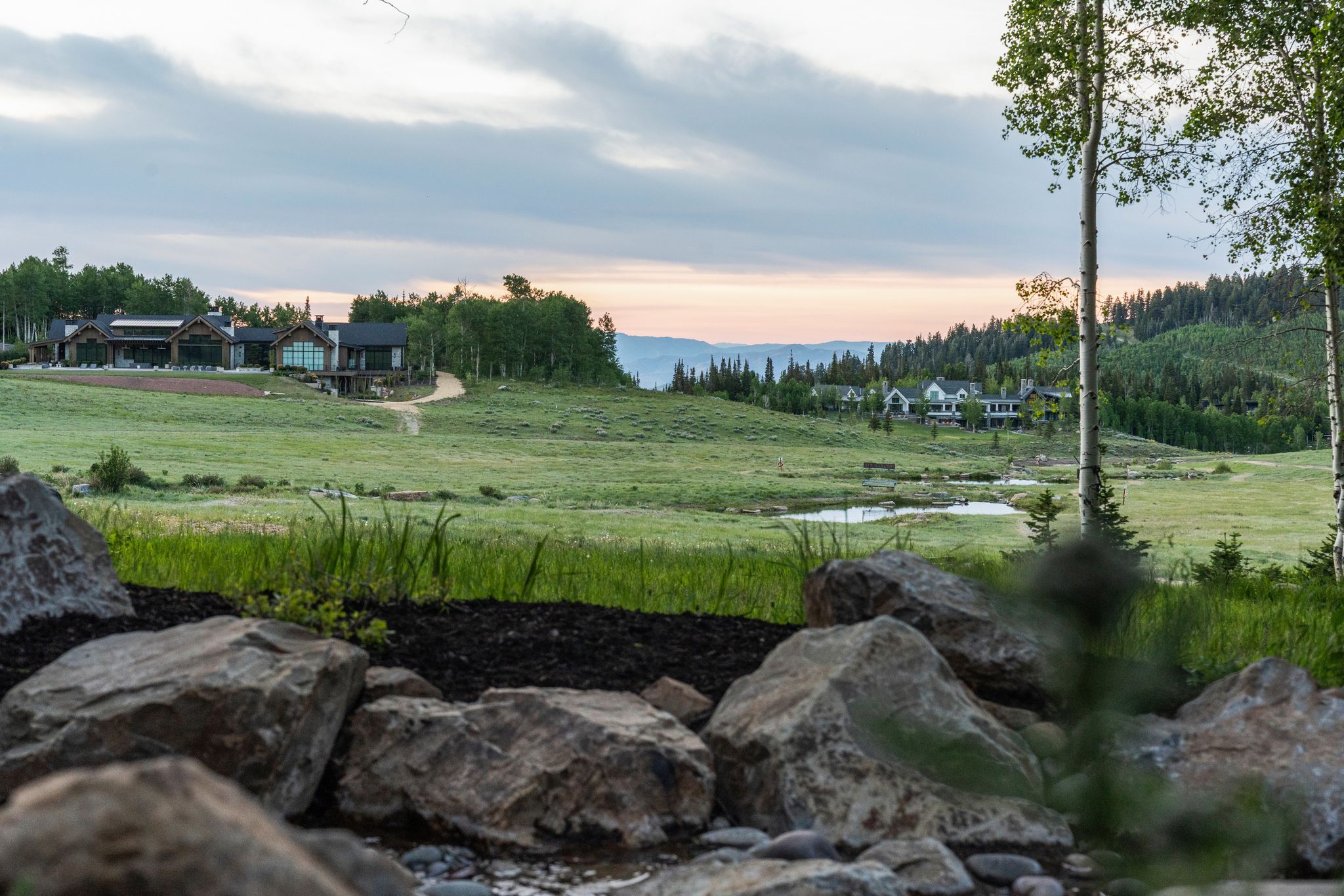 Expansive natural landscape featuring a pond, mature trees, and mountainous terrain