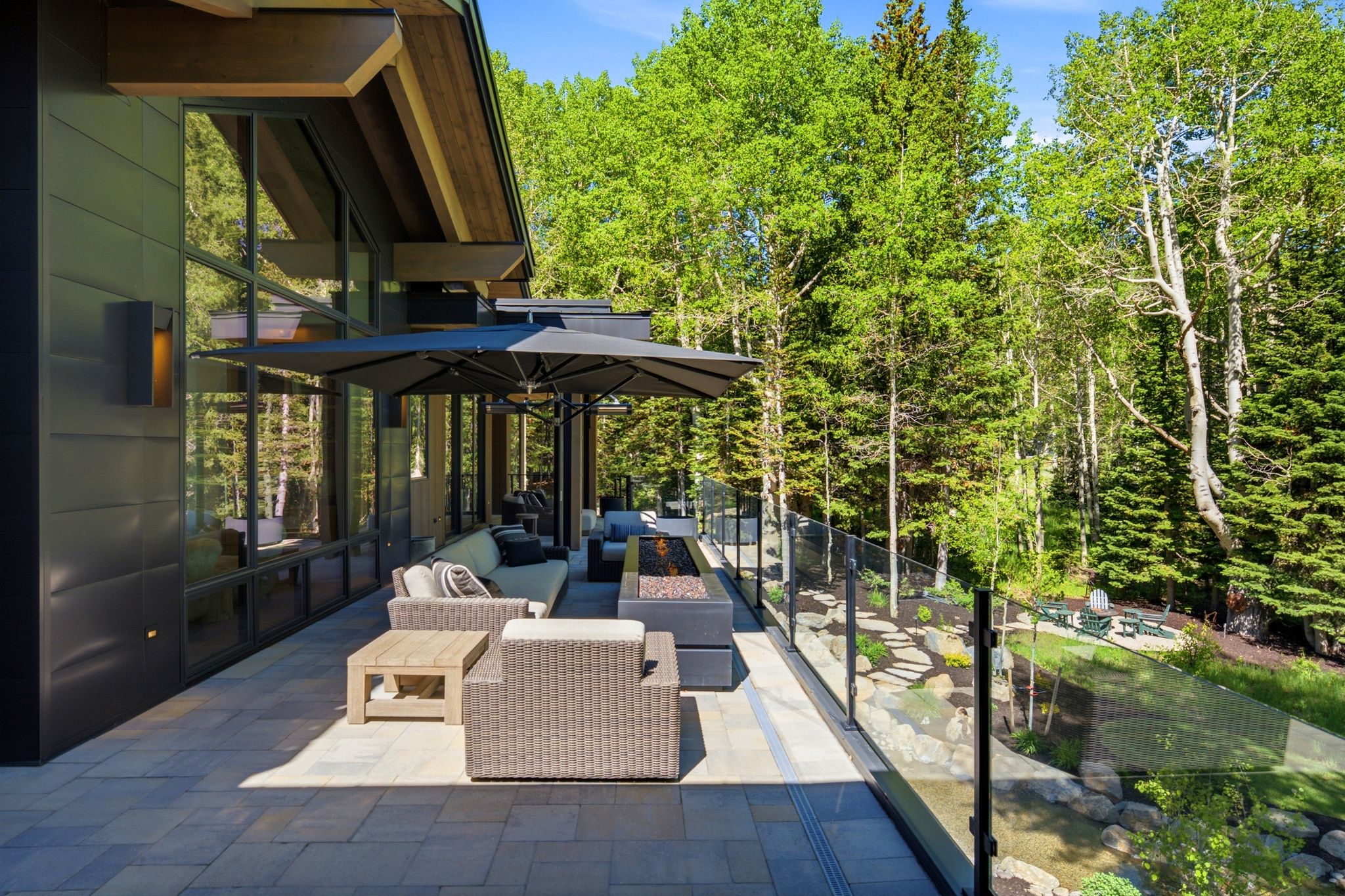 Expansive outdoor patio featuring paver flooring, a linear fire pit, and a glass safety railing