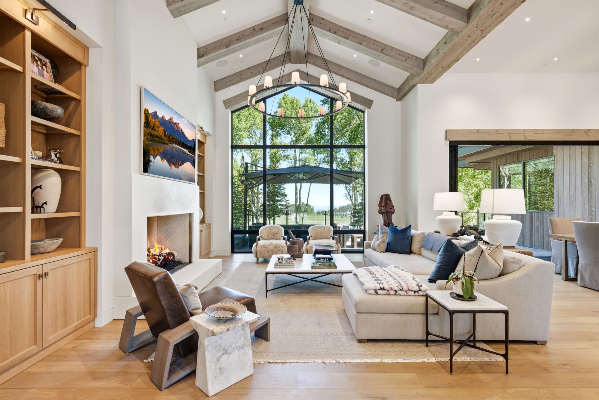 Vaulted ceiling with exposed wood beams, expansive floor-to-ceiling windows, built-in fireplace, and wood-finish flooring