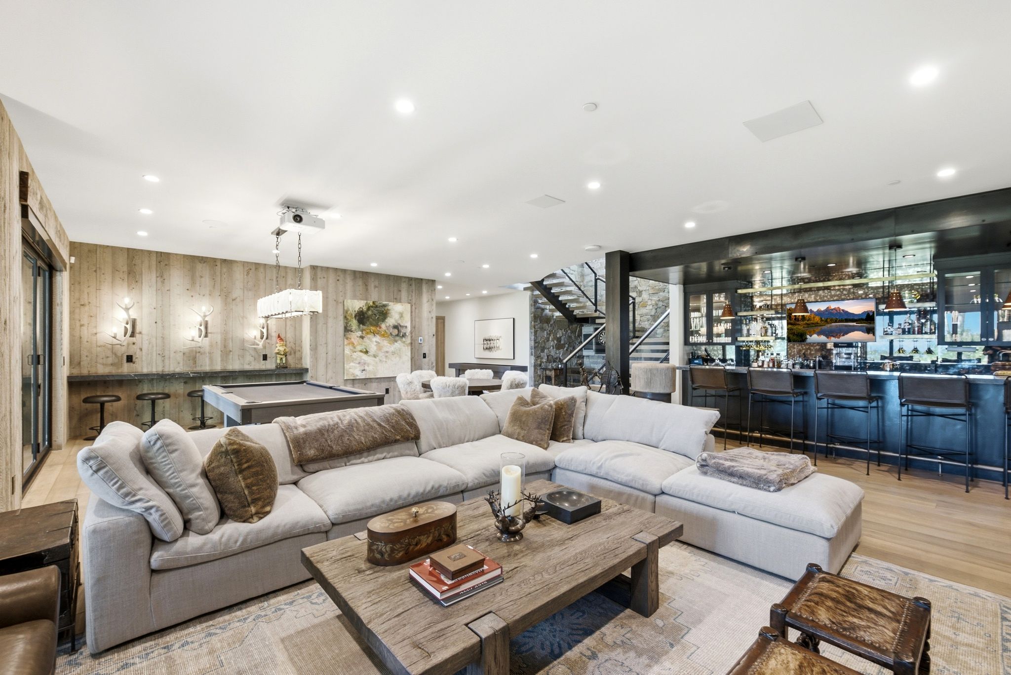 Spacious entertainment room featuring a custom full-service bar, wood-finish flooring, recessed lighting, and a projector