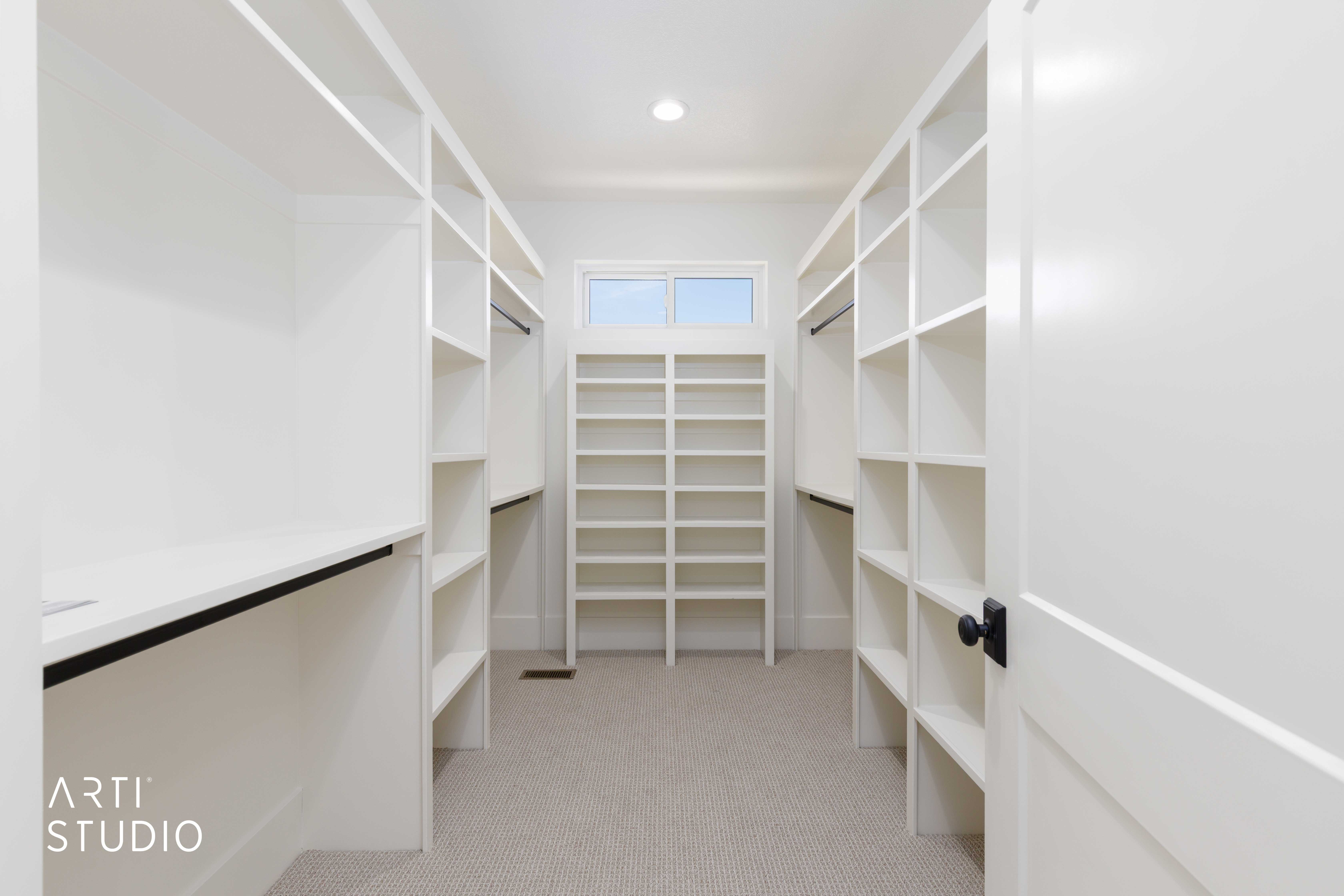 Spacious custom closet featuring extensive white built-in shelving, integrated hanging rods, and light-colored carpet flooring