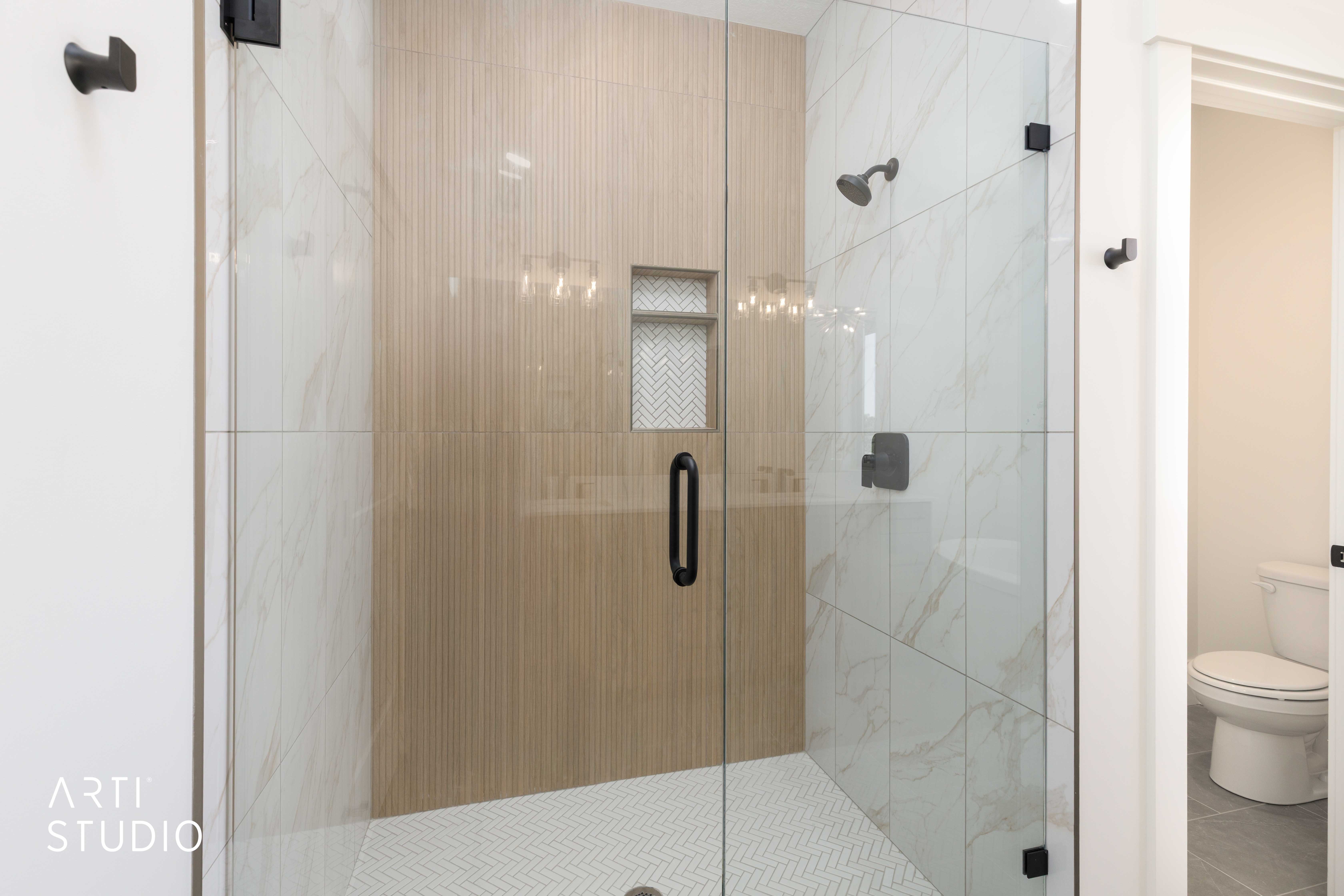 Glass-enclosed shower featuring white herringbone tile flooring, large-format marble-look wall tiles, and a recessed niche with herringbone tile