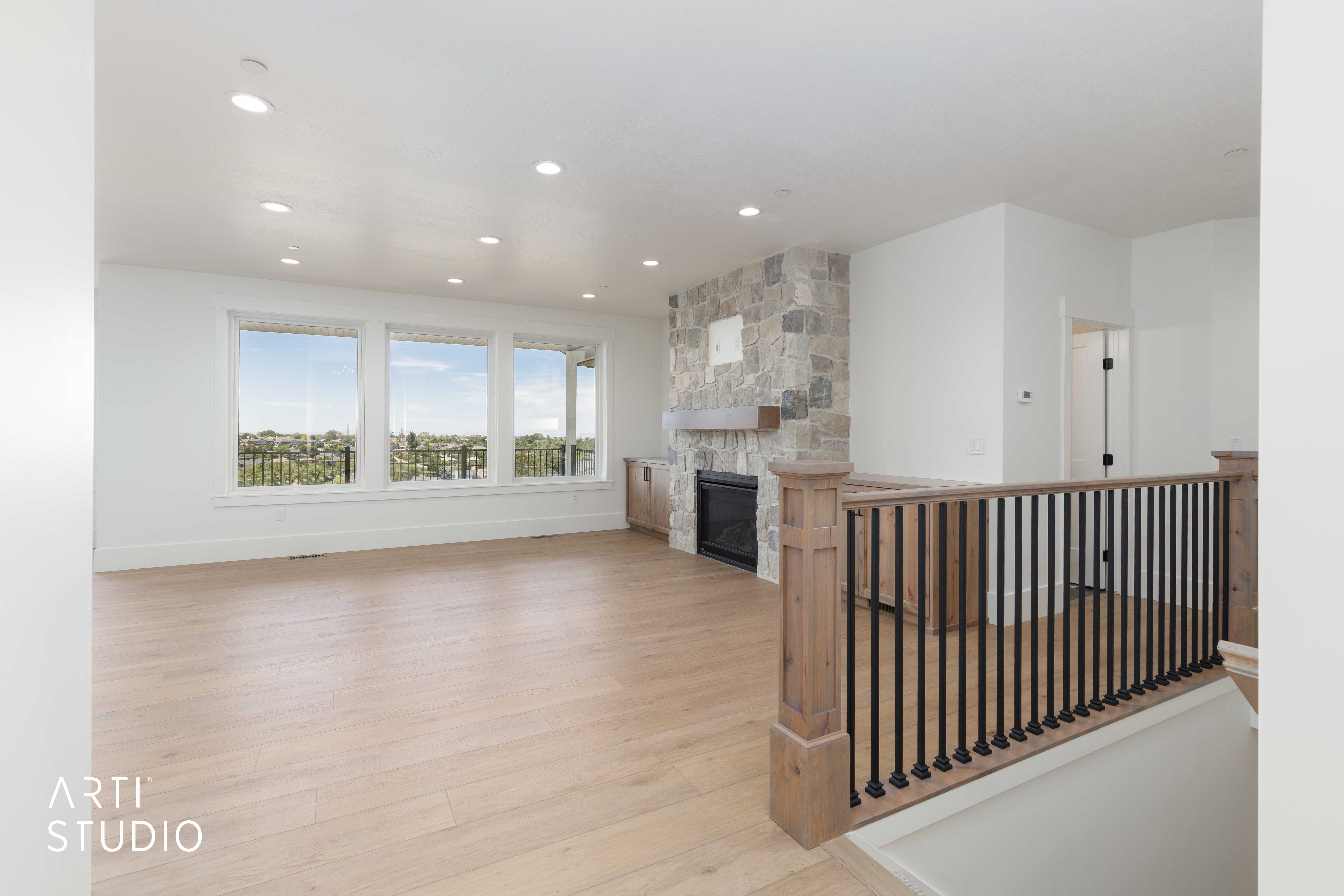 Spacious living area featuring light wood-finish flooring, a stone-clad fireplace with a wood mantle and built-in cabinetry, large windows offering expansive scenery, and recessed lighting