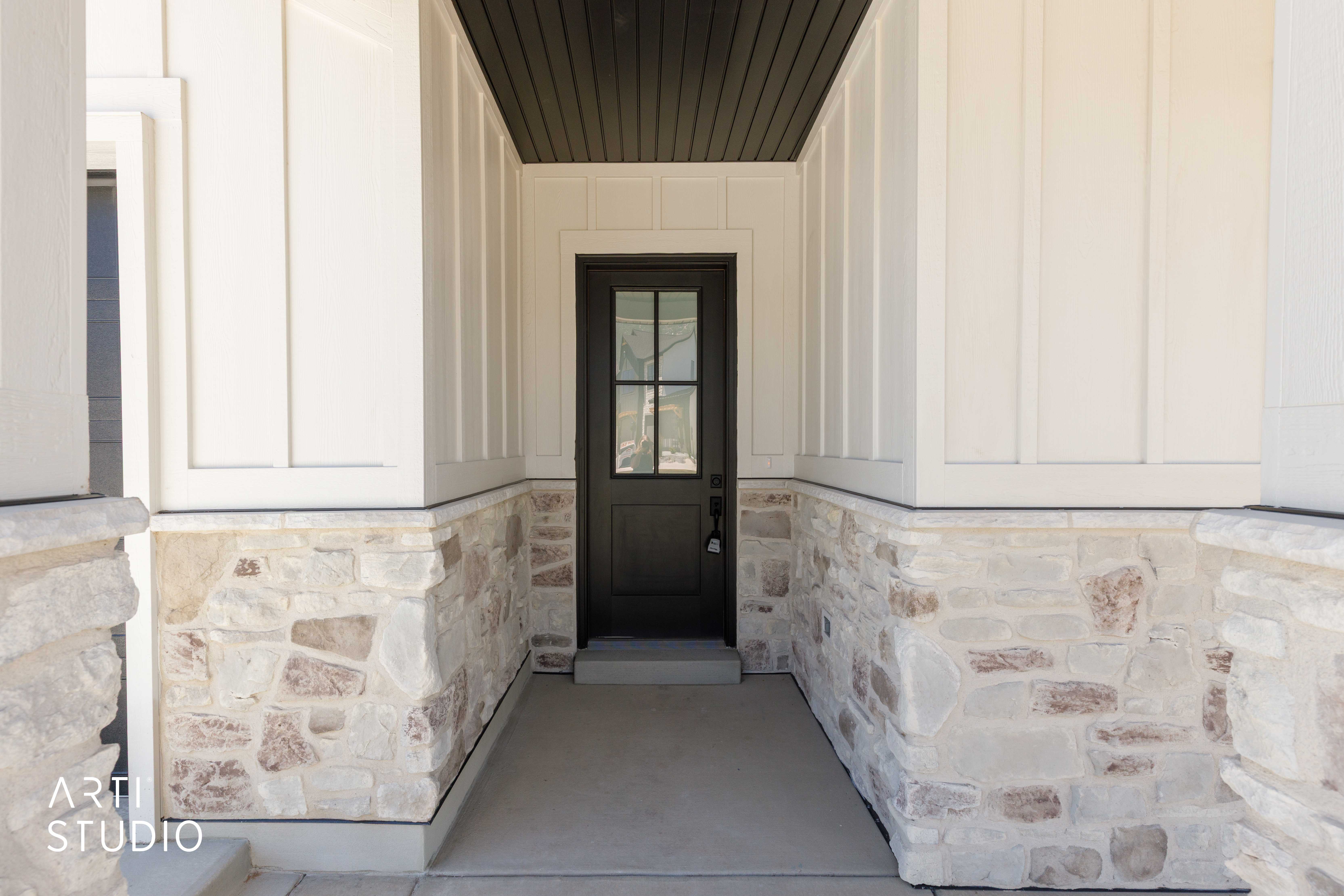 Covered entry featuring a dark-toned door with glass lites, stone veneer accents, vertical board-and-batten siding, and a dark-toned soffit