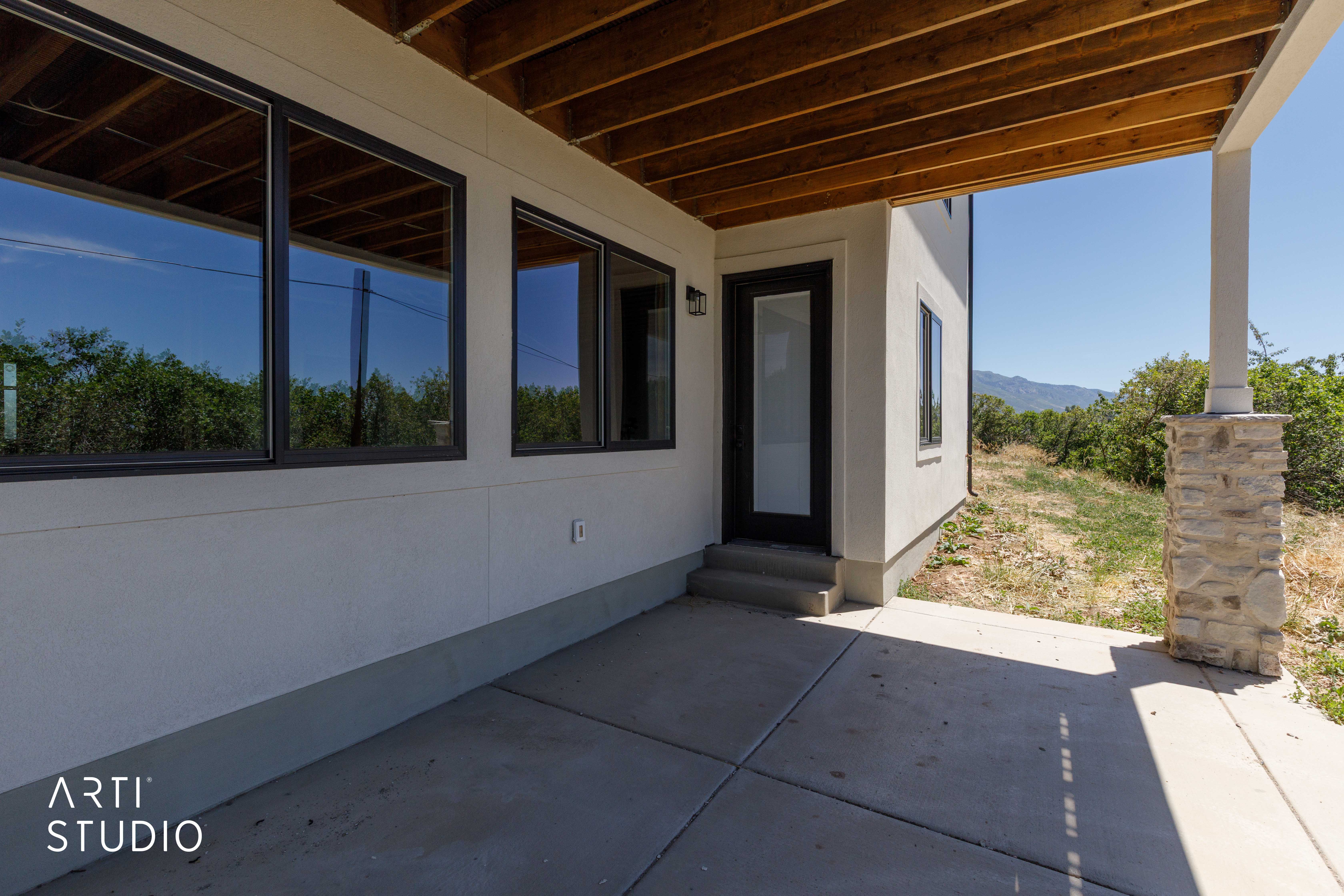 Covered concrete patio featuring a wood-finished ceiling, stone-accented support column, and multiple large windows