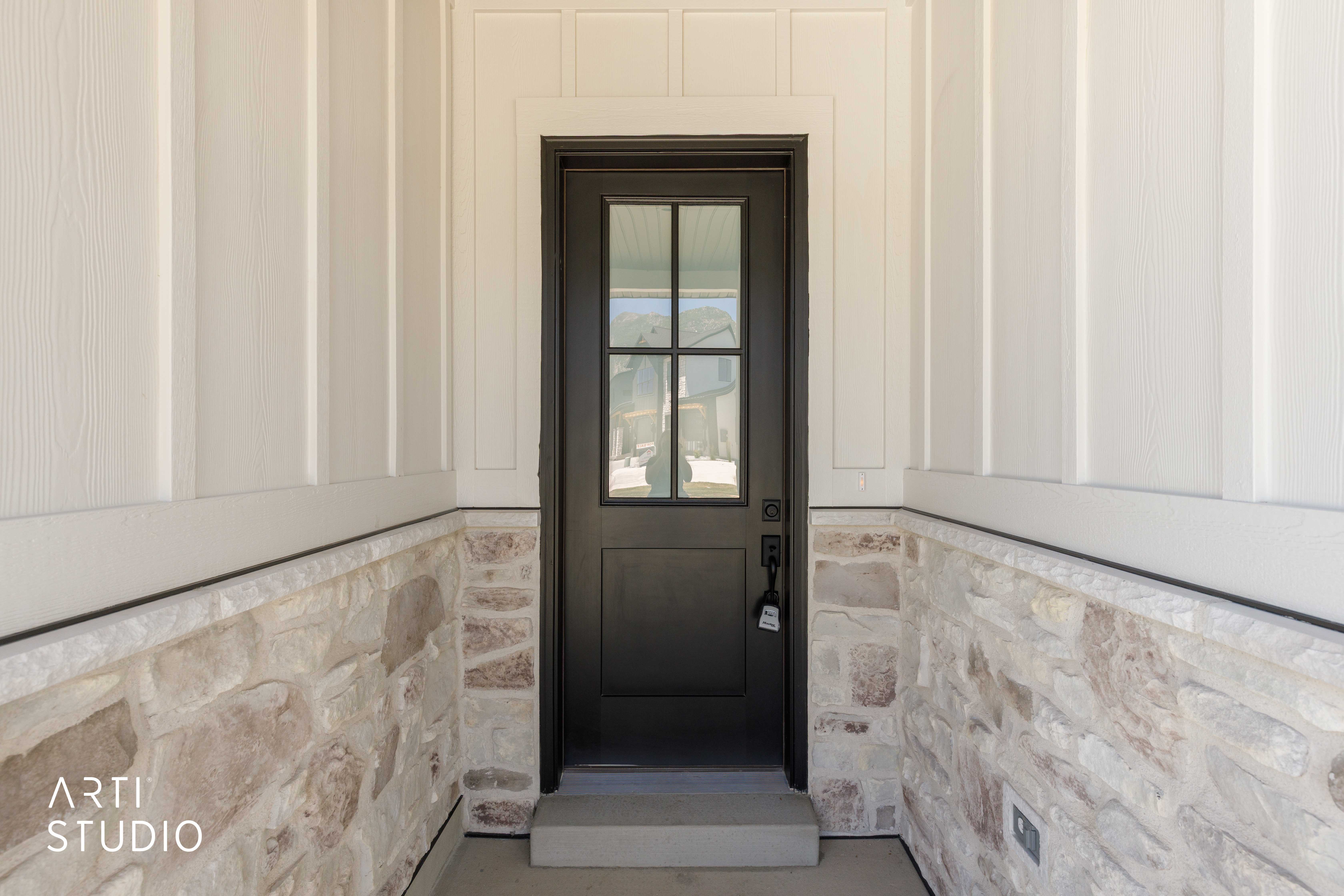Modern black front door with clear glass panels, framed by white board and batten siding