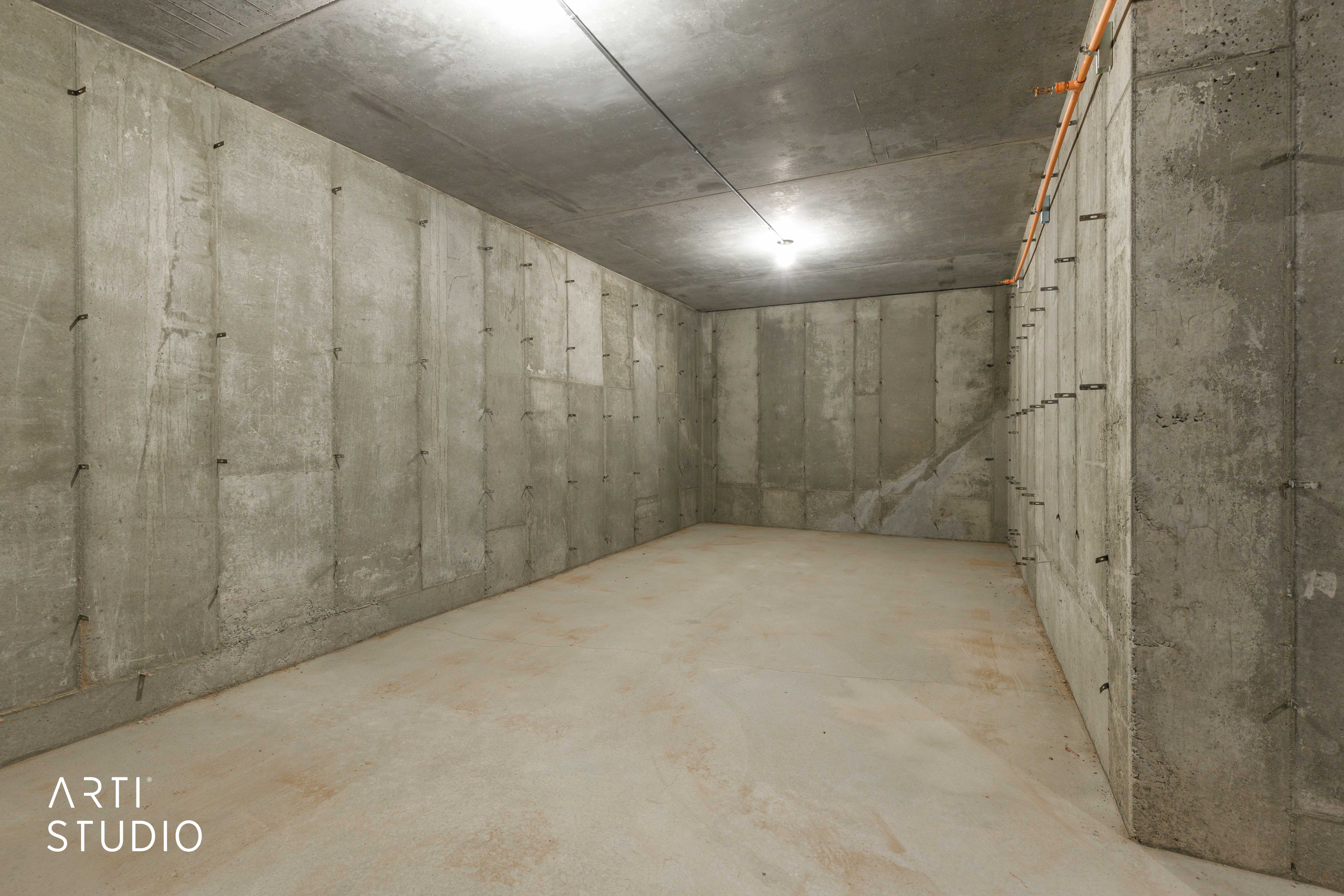 Concrete walls and ceiling featuring exposed wiring and a single overhead light fixture