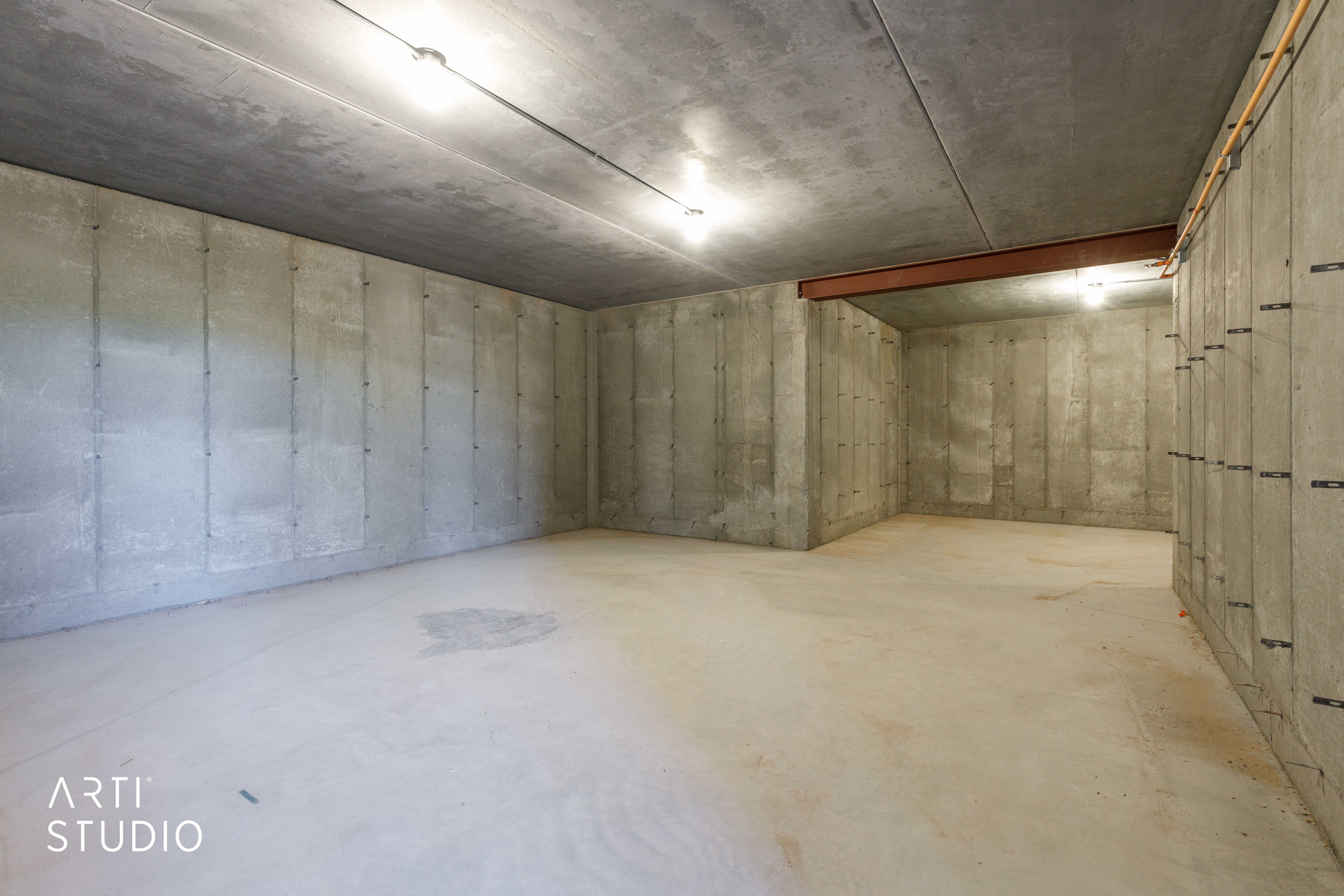 Spacious concrete room featuring concrete walls, concrete flooring, concrete ceiling, track lighting, and exposed structural beam