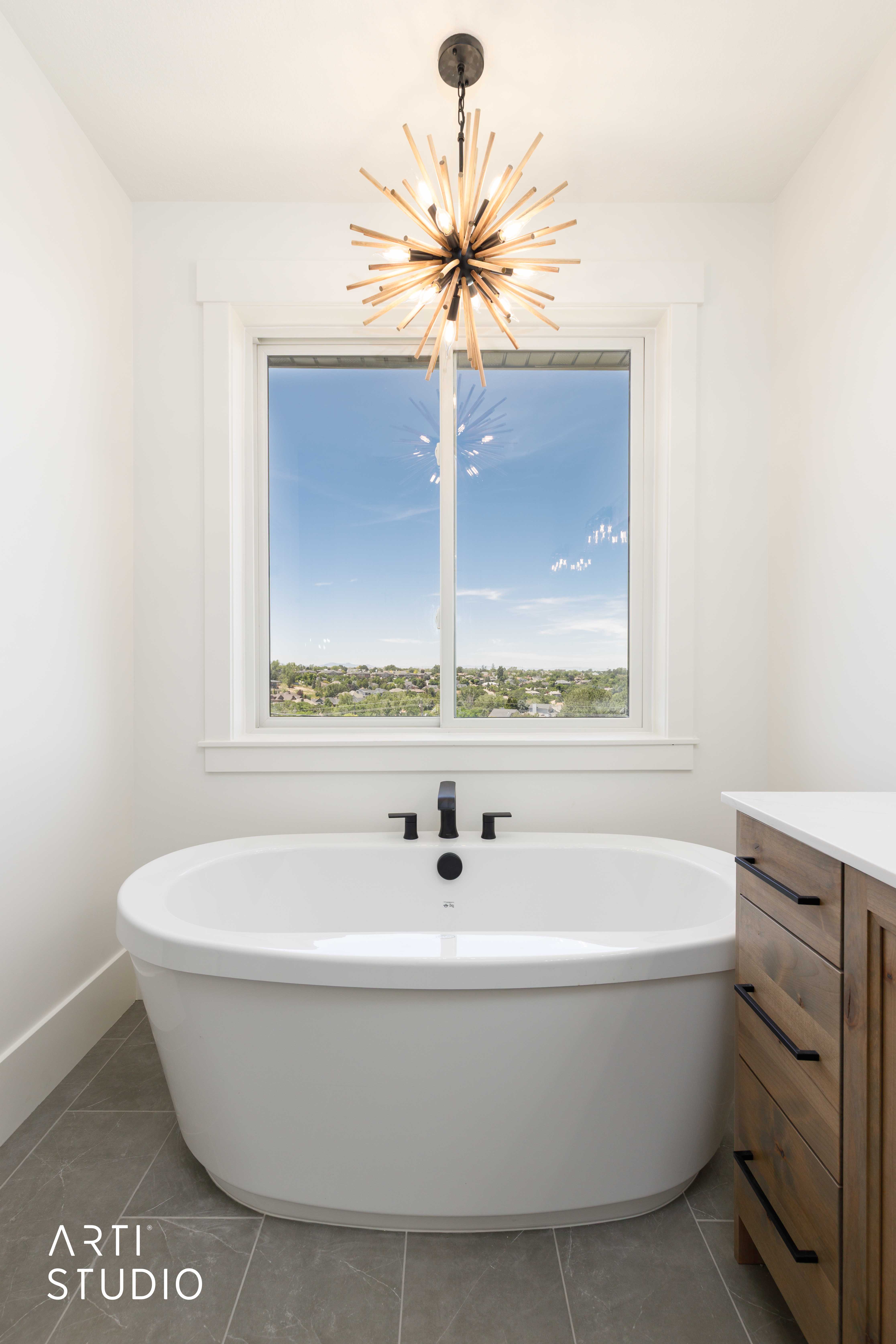 Freestanding oval soaking tub with matte black fixtures, set against a window with a broad sill