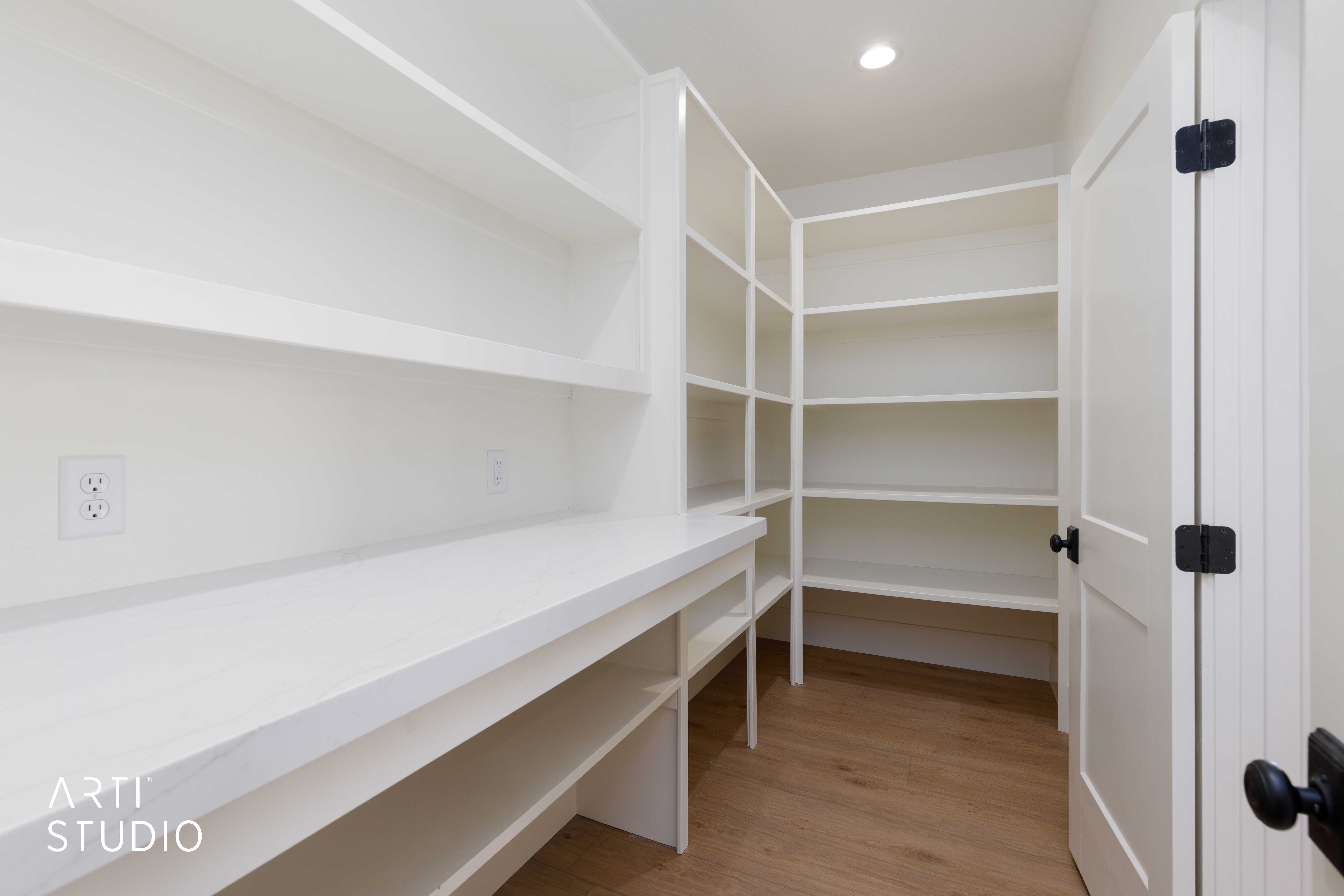 Built-in pantry featuring extensive white shelving, a solid white countertop, wood-finish flooring, recessed lighting, and a white paneled door with matte black hardware