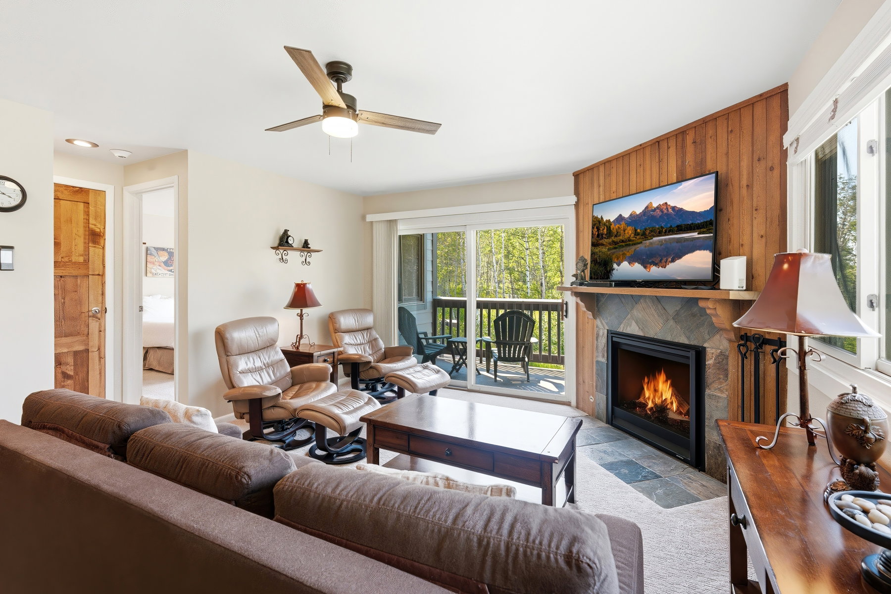 Living area featuring a stone-clad fireplace with a wood mantle, wood-paneled accent wall, and a ceiling fan