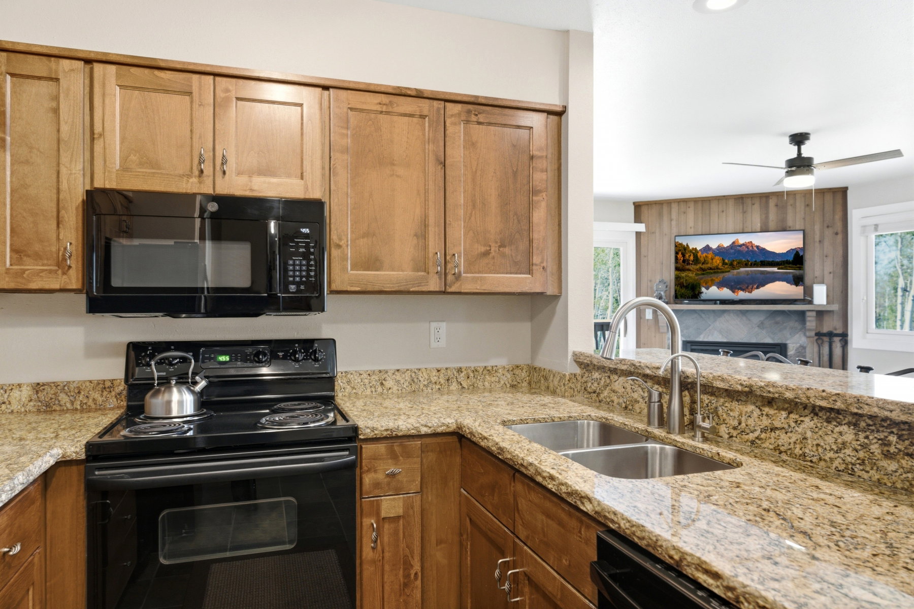 Kitchen featuring light wood cabinetry, stone-finish countertops, black electric range, and an over-range microwave