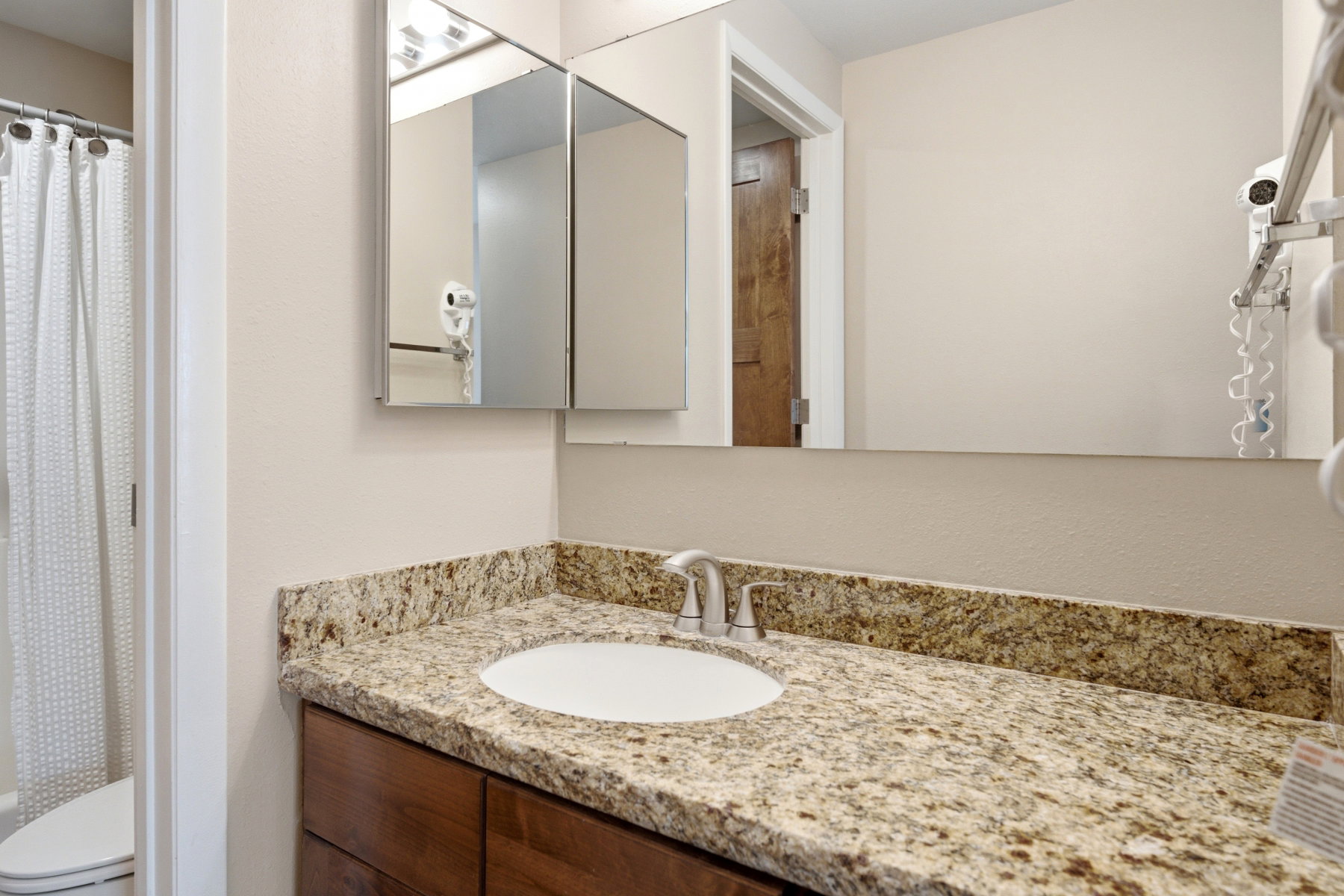 Bathroom vanity featuring a speckled countertop, undermount sink with chrome faucet, and wood-finish cabinetry