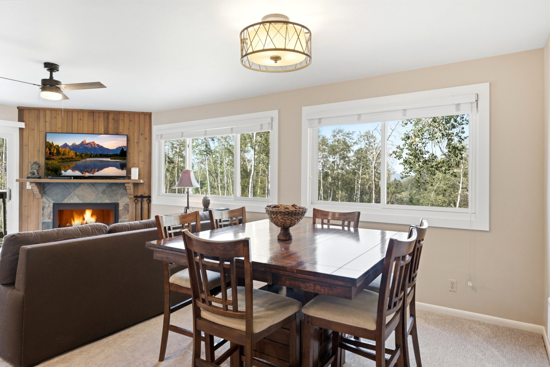 Open-concept living space with a stone-surround fireplace, wood panel accent wall, and multiple windows