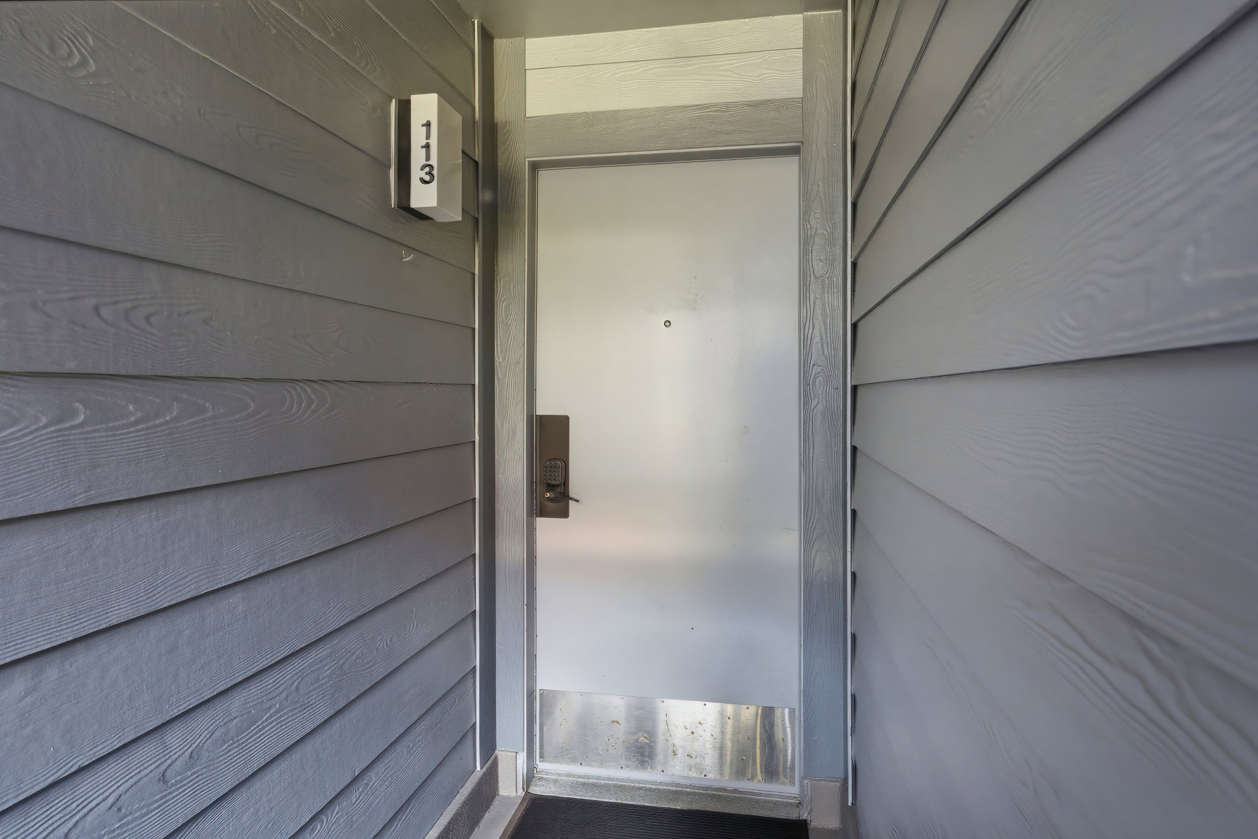 Entryway featuring horizontal siding, a light gray door frame, a frosted privacy door, and a dark entry mat