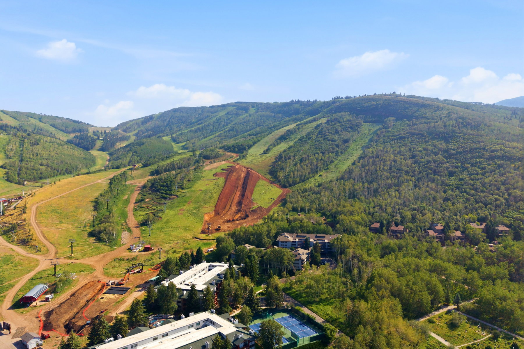 Expansive mountainous landscape featuring lush green slopes, wooded areas, and multiple structures
