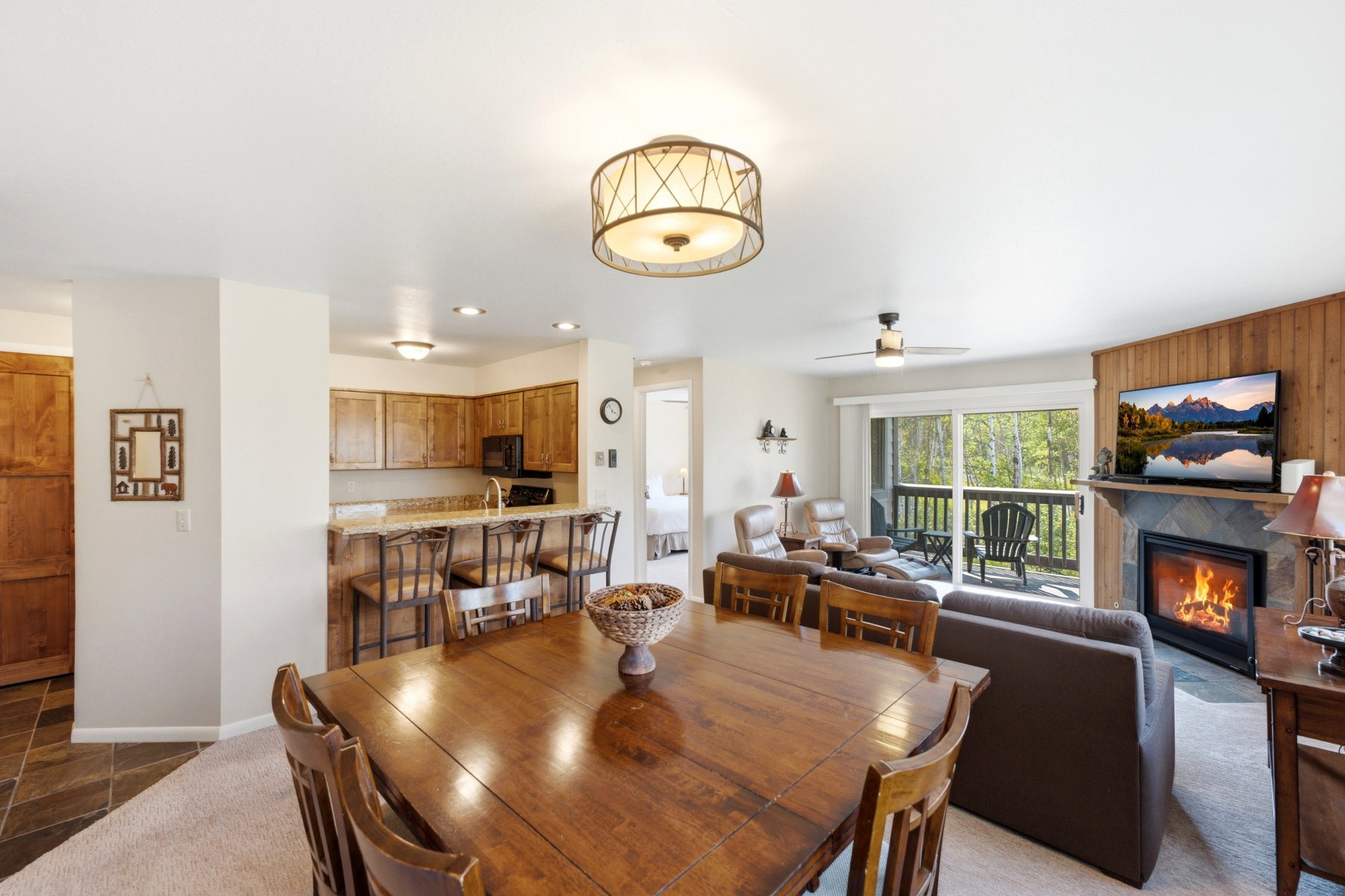 Open-concept living area featuring a kitchen with breakfast bar, dining space, and a living room with a stone fireplace and wood paneling