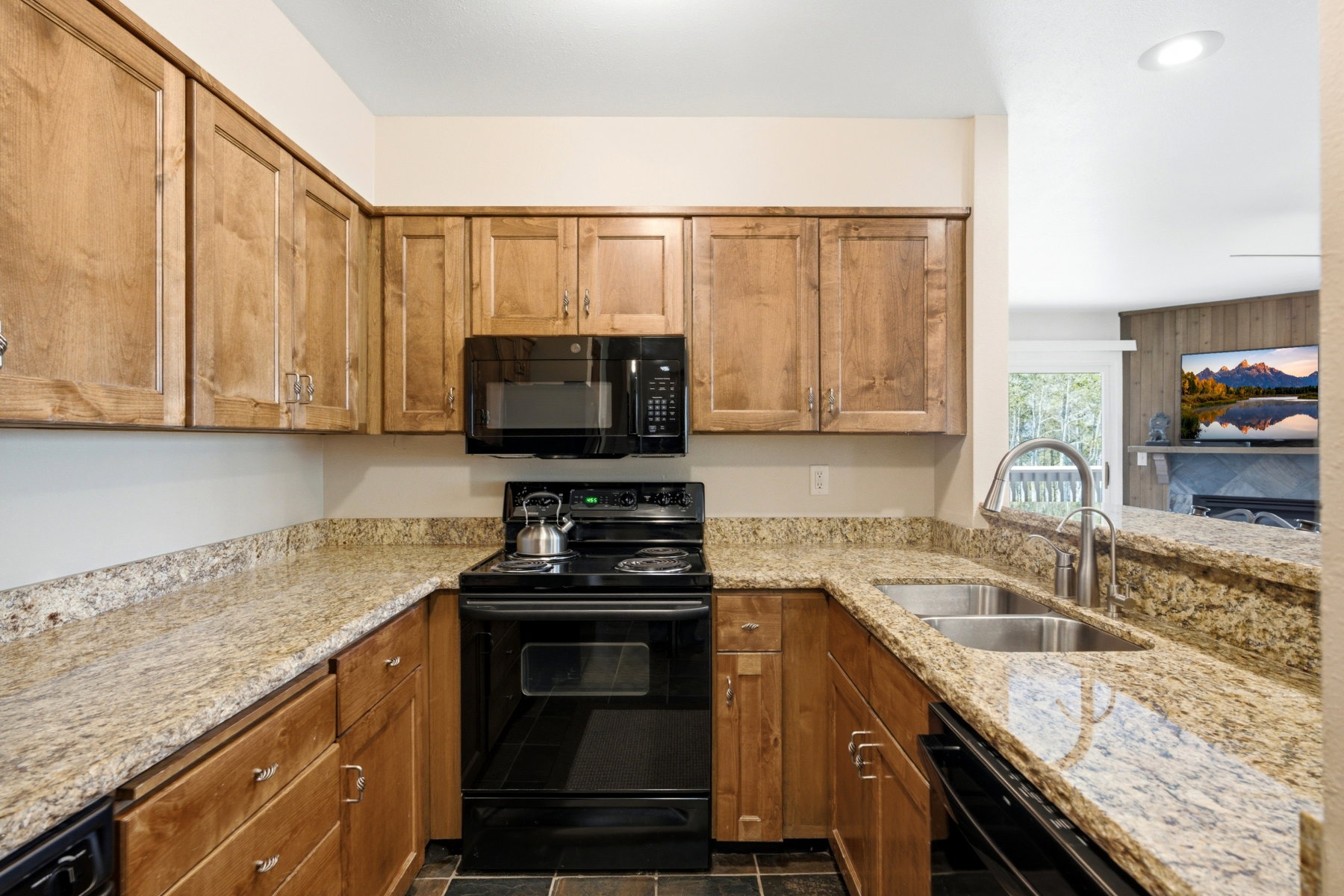 U-shaped kitchen featuring wood cabinetry, speckled countertops, black appliances, and a double basin sink with a high-arch faucet