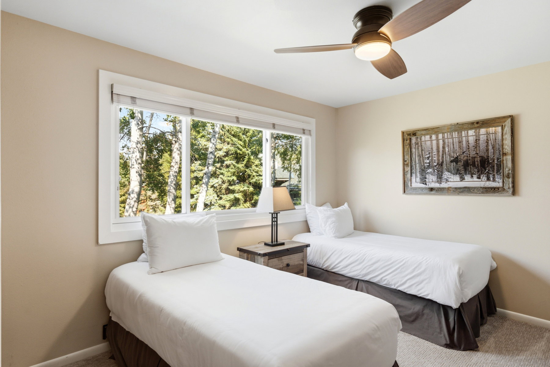 Interior room featuring a large horizontal window with white trim, a dark wood-finish ceiling fan with integrated lighting, neutral wall paint, and light-colored carpeting