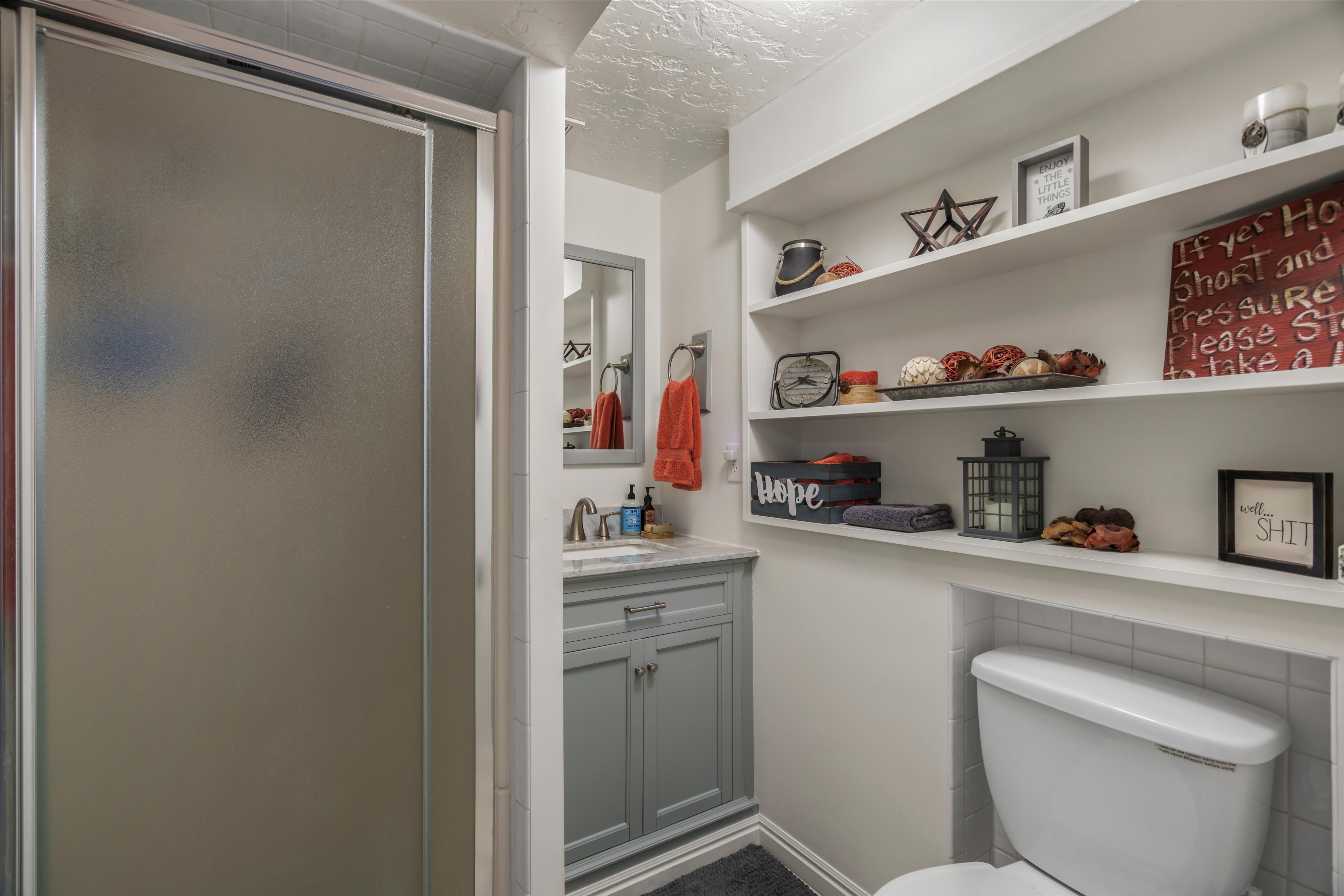 Frosted glass shower enclosure, blue vanity with countertop, frameless mirror, and integrated shelving
