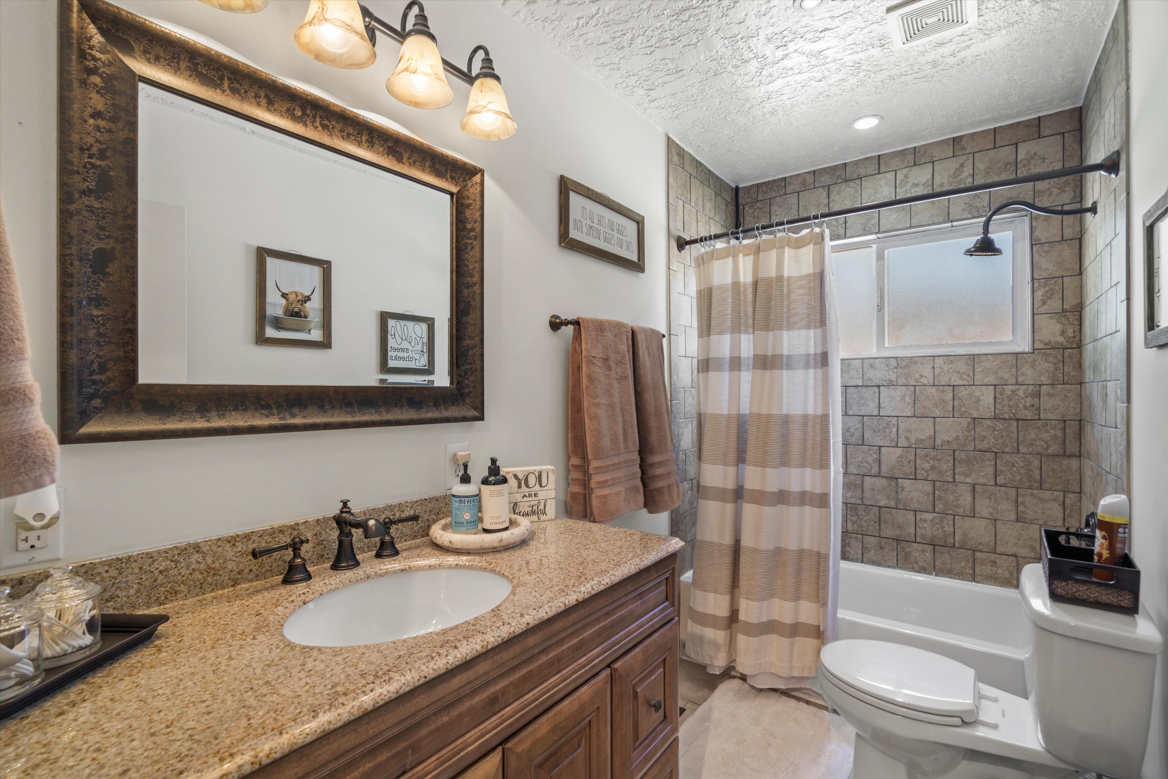 Bathroom featuring countertop, dark wood-finish vanity, large framed mirror, and a tiled shower-tub combination with a frosted window