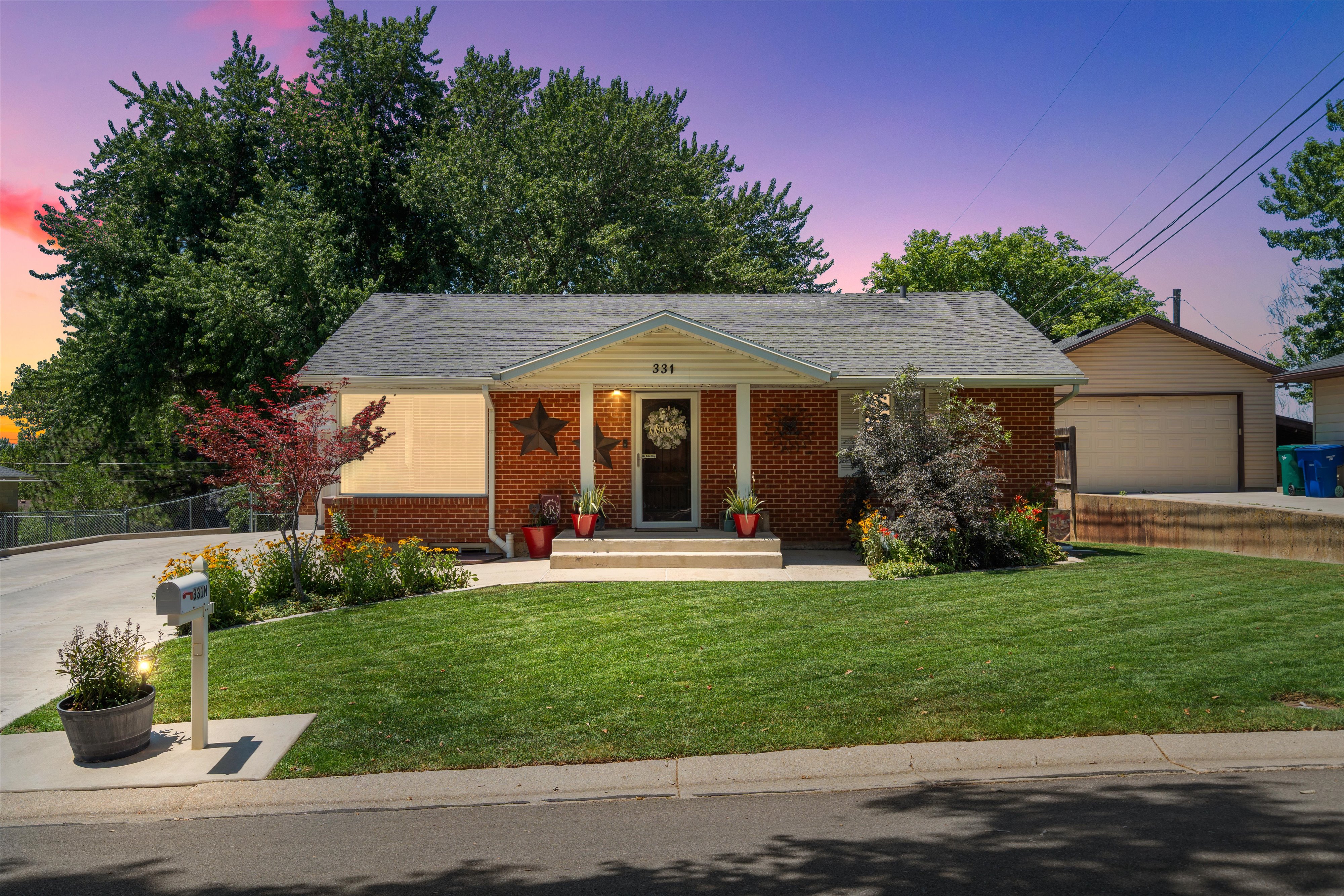 Brick facade home featuring a peaked roofline, front porch, and mature landscaping