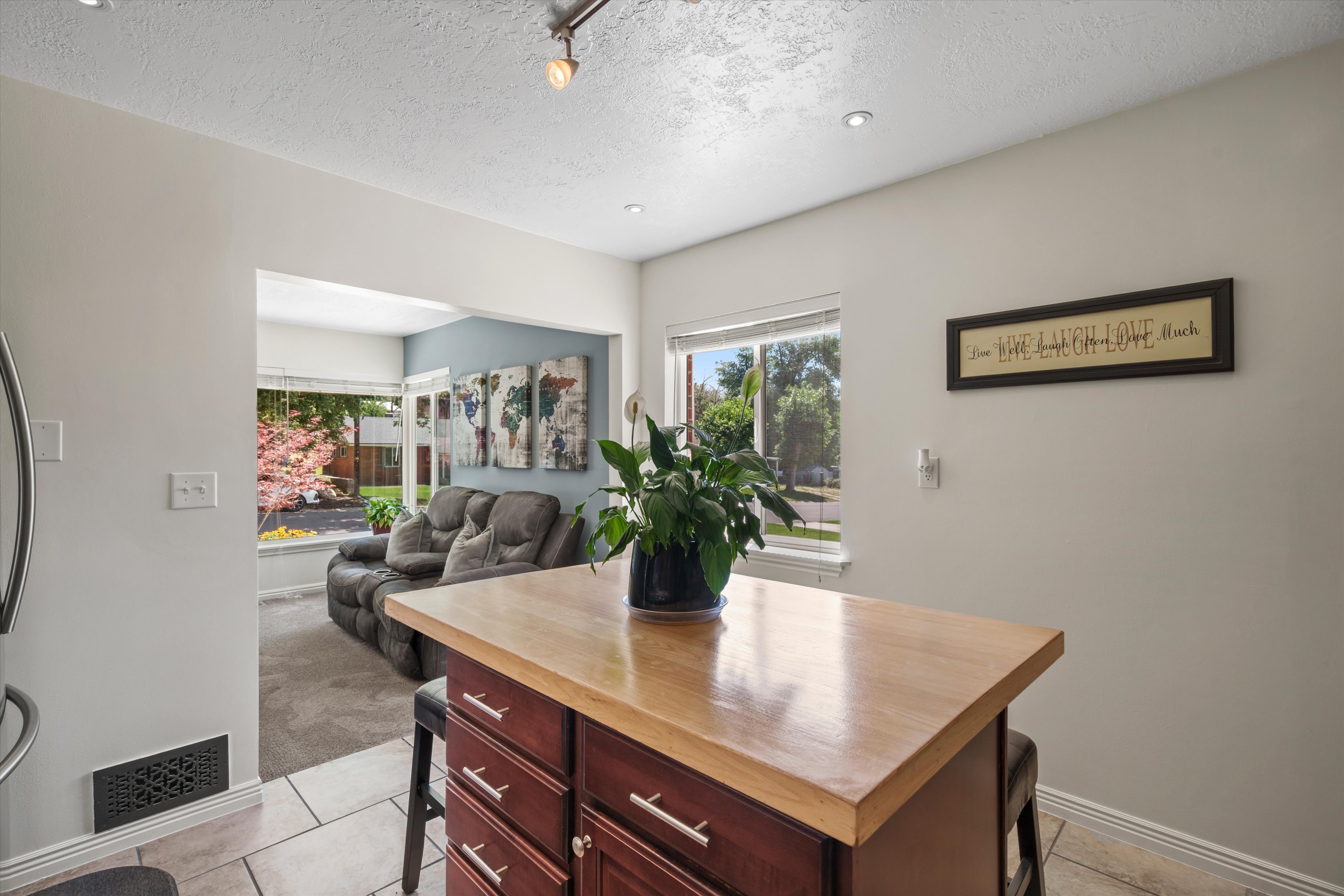 Kitchen island with wood-finish countertop, tile flooring, recessed lighting, and a pass-through opening to a Living room